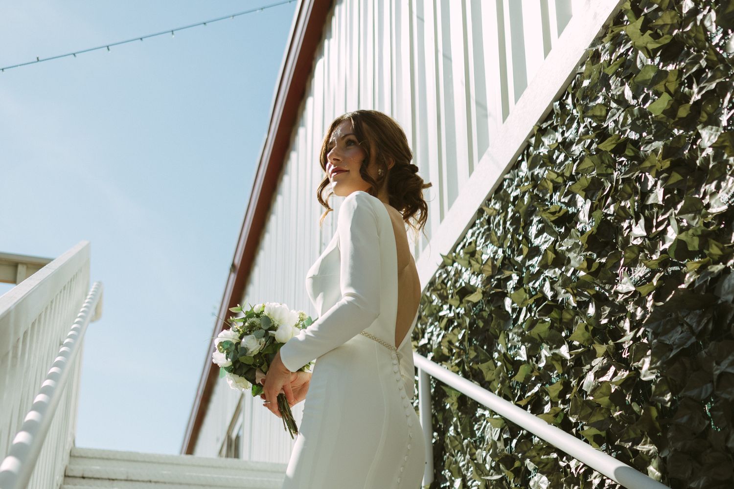 A person in a white dress walks through a garden path with hanging white curtains creating an ethereal atmosphere.