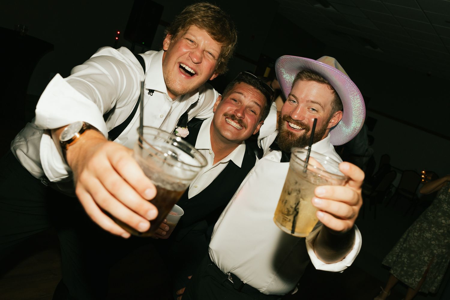 Three party guests in formal attire raise their drinks for a celebratory toast.