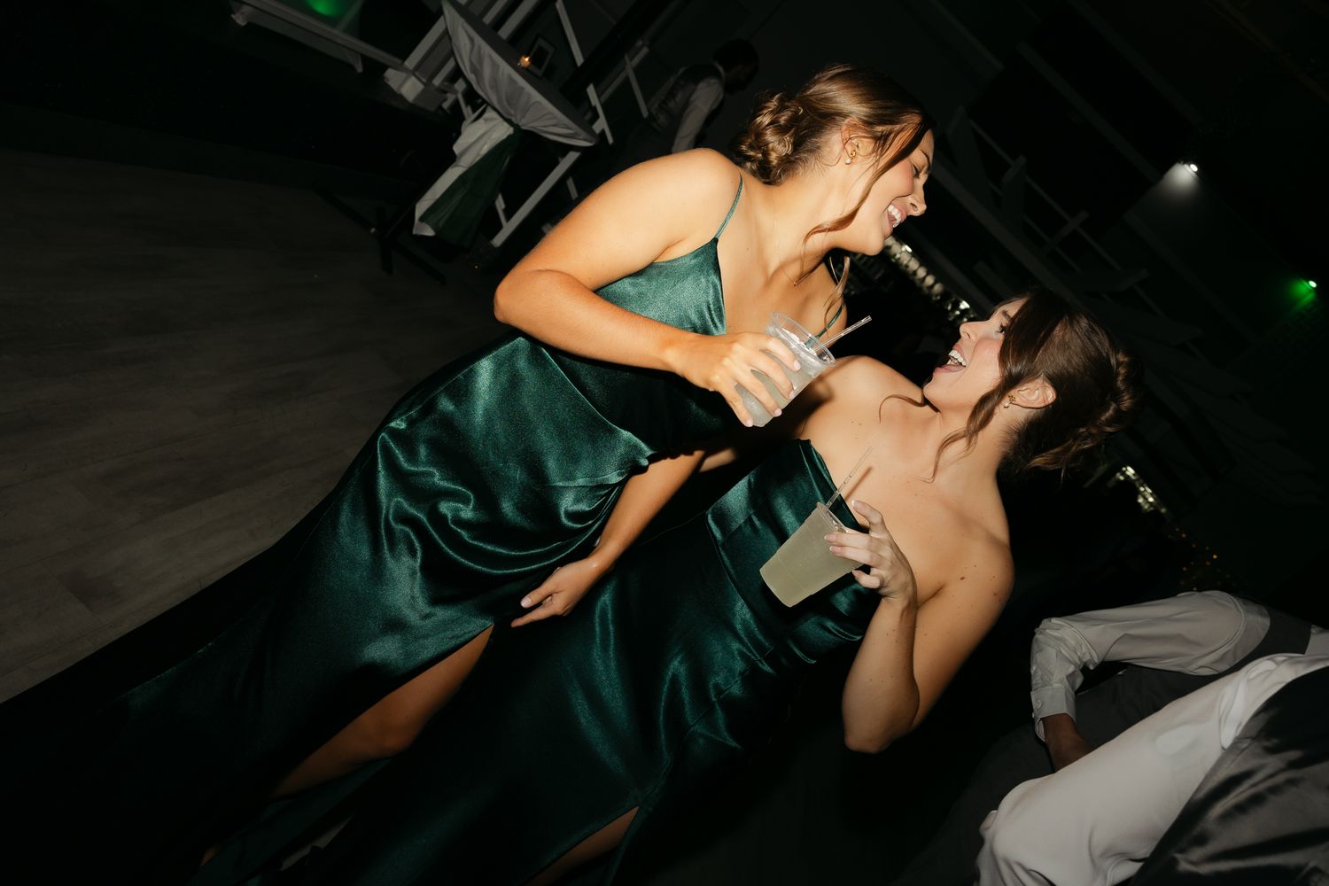 Two guests in formal attire sharing drinks and laughter at an evening celebration.