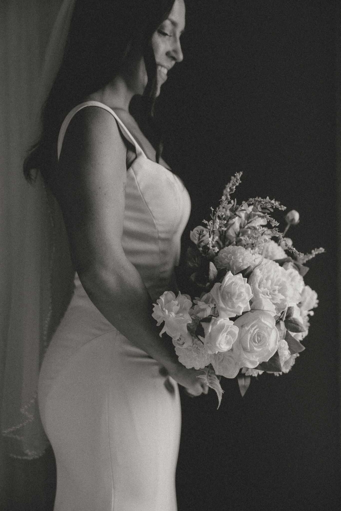 Black and white portrait of bride holding white rose bouquet in fitted wedding dress.