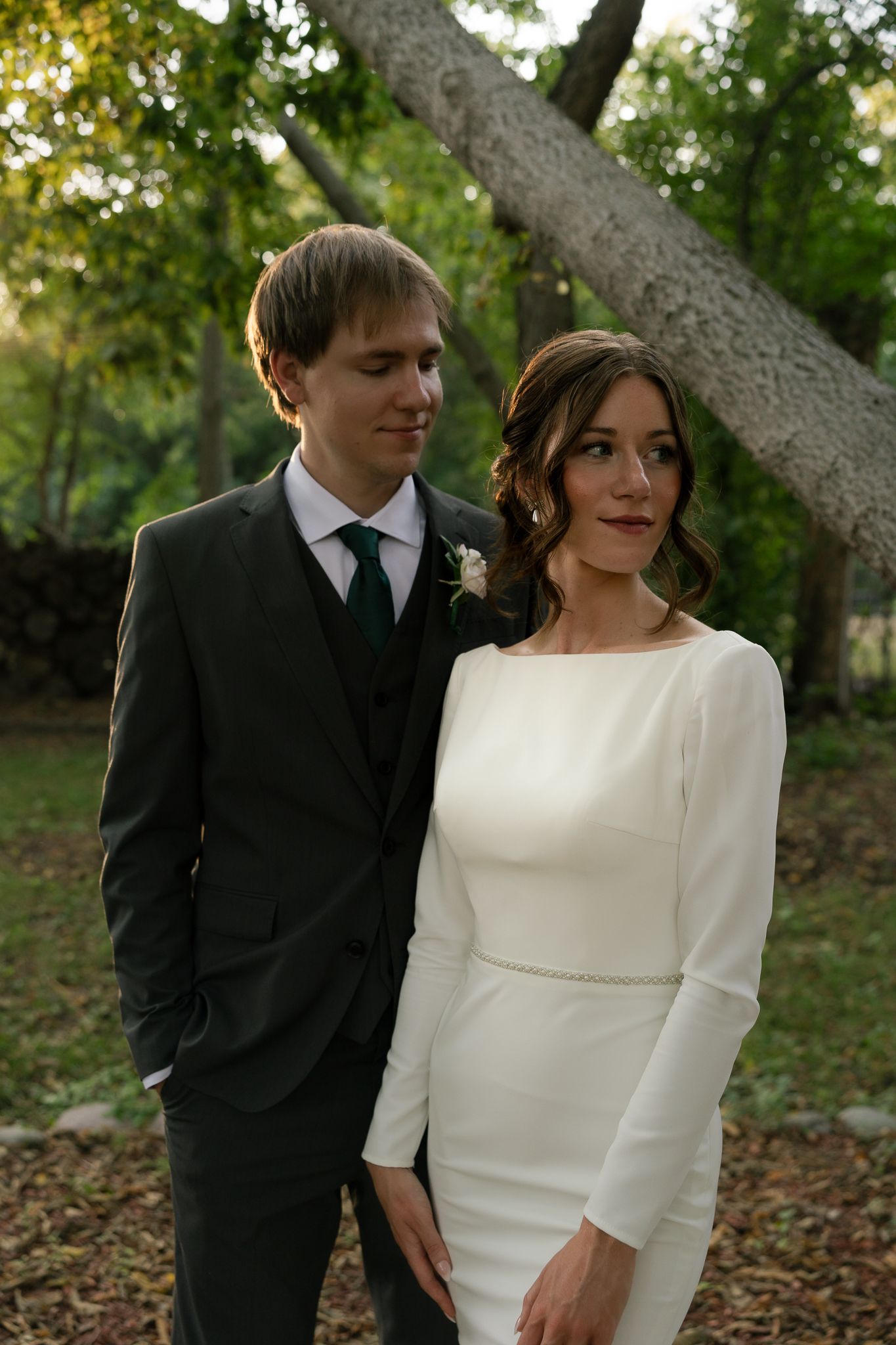 A couple shares a tender moment in their wedding attire among autumn trees.