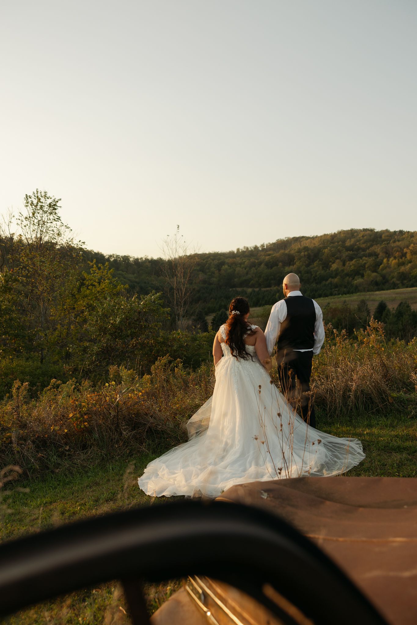 Sunset wedding portrait with couple walking along mountain path as dress trails behind.