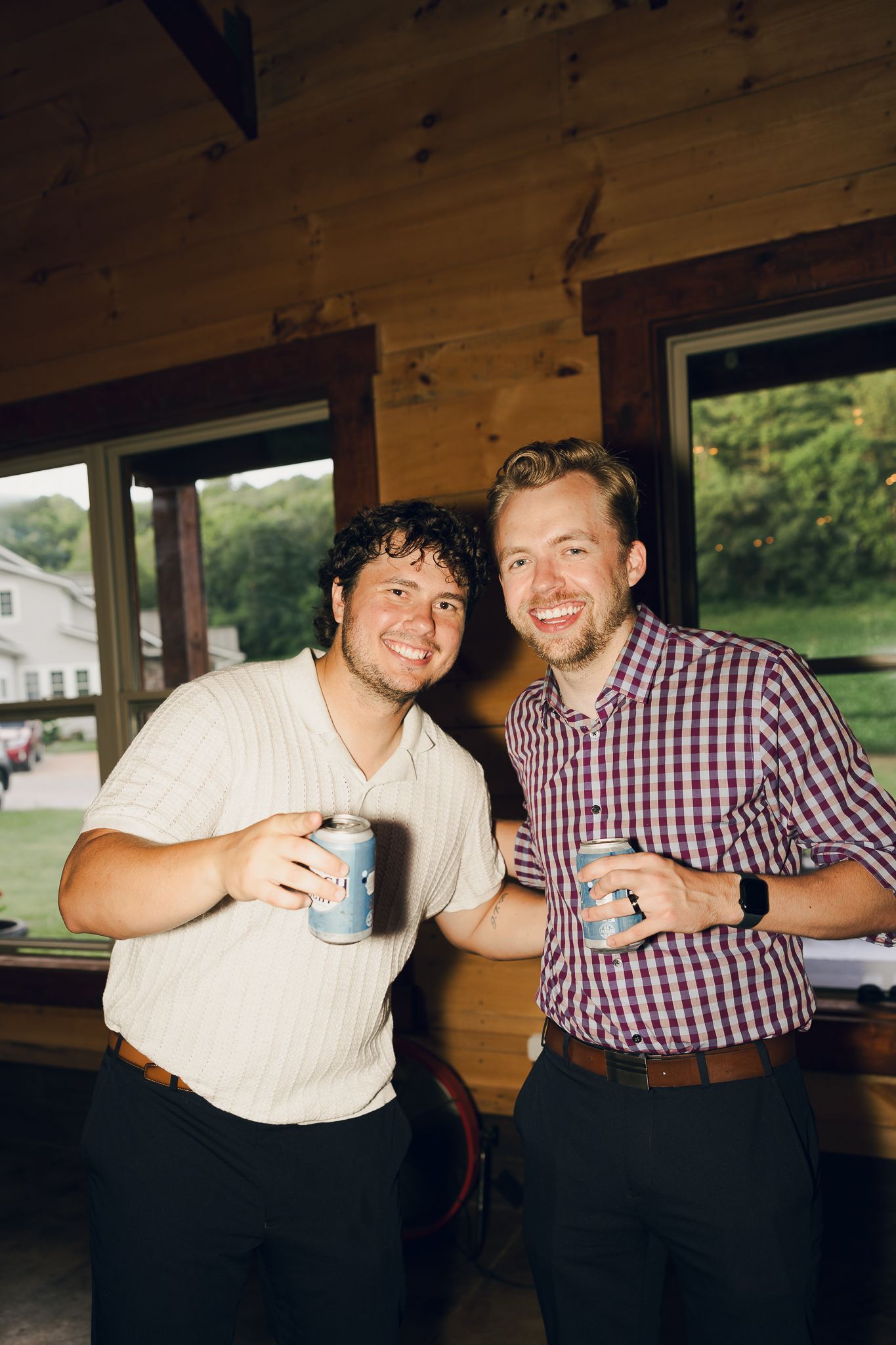 Friends enjoying drinks and laughter at a rustic wooden bar during a wedding celebration.