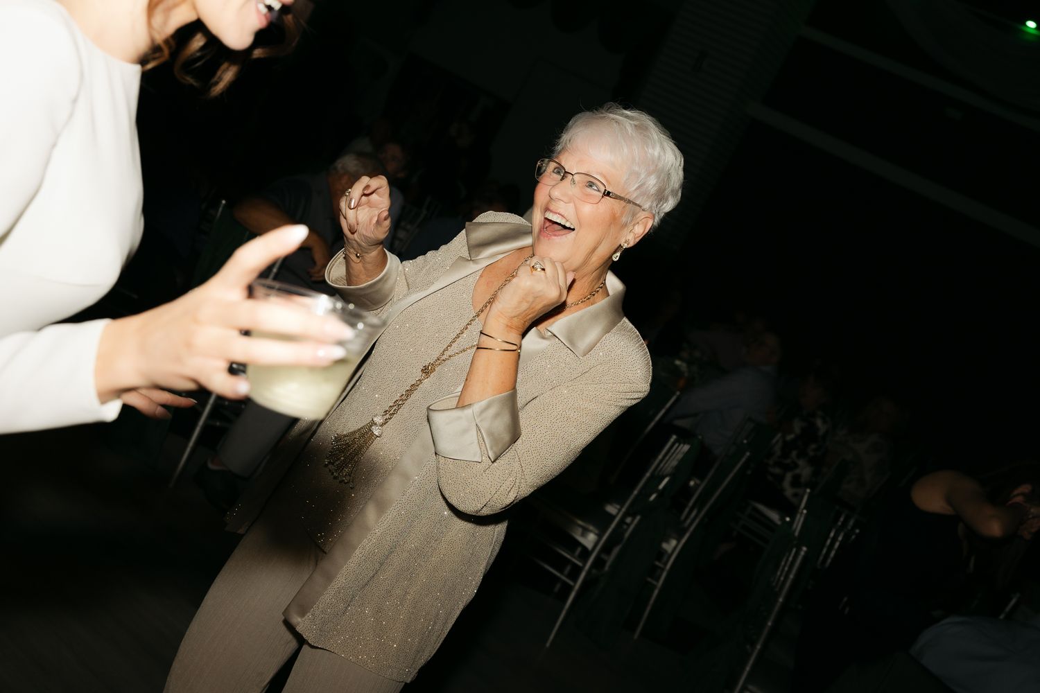 Party guests enjoying drinks and laughter at a dimly lit reception.