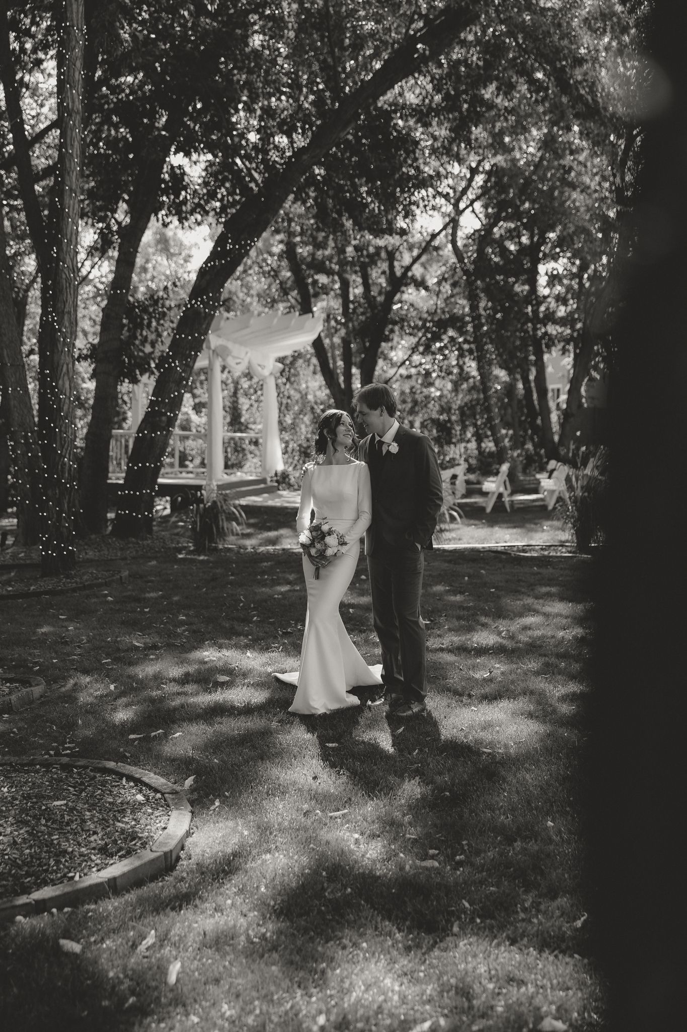 A black and white wedding photo captures a couple in a serene wooded setting.
