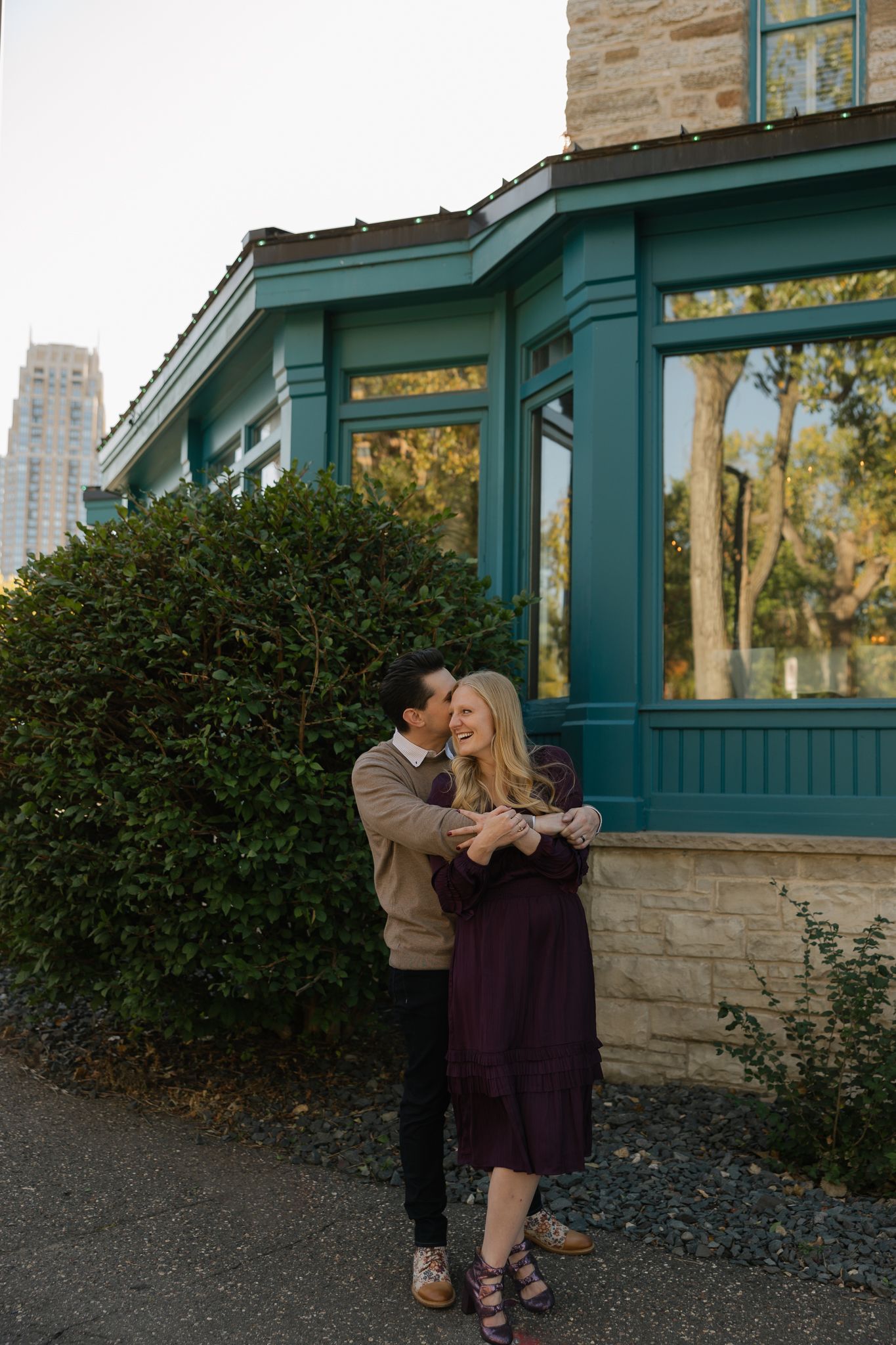 Romantic couple embracing outside a stone building with green architectural details.
