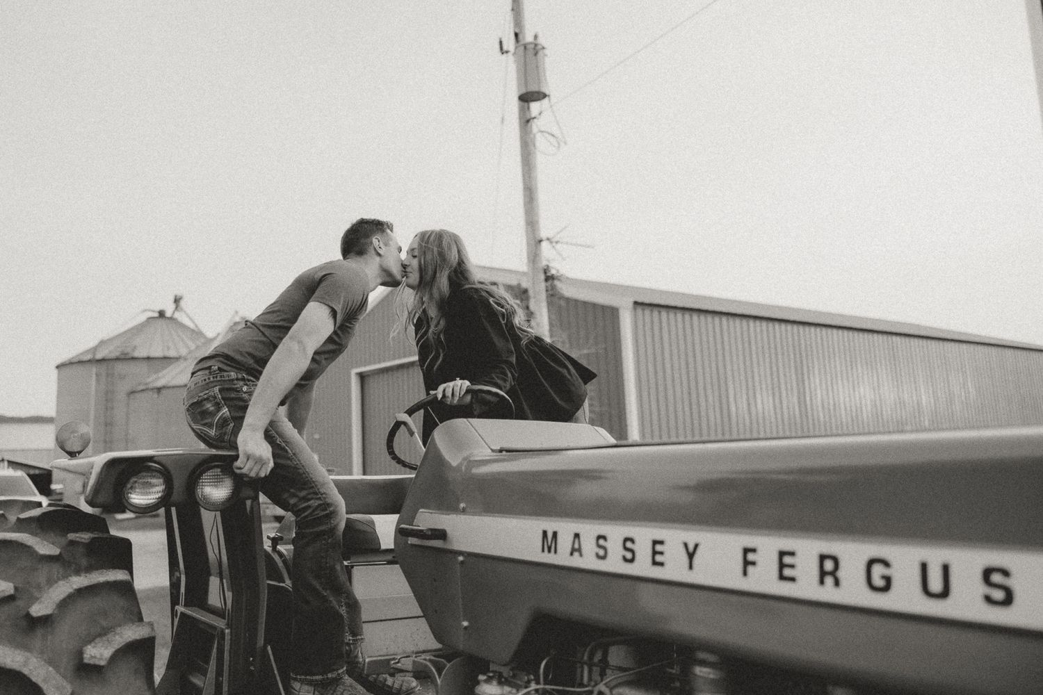 A couple shares a romantic moment on a vintage Massey Ferguson tractor in black and white.