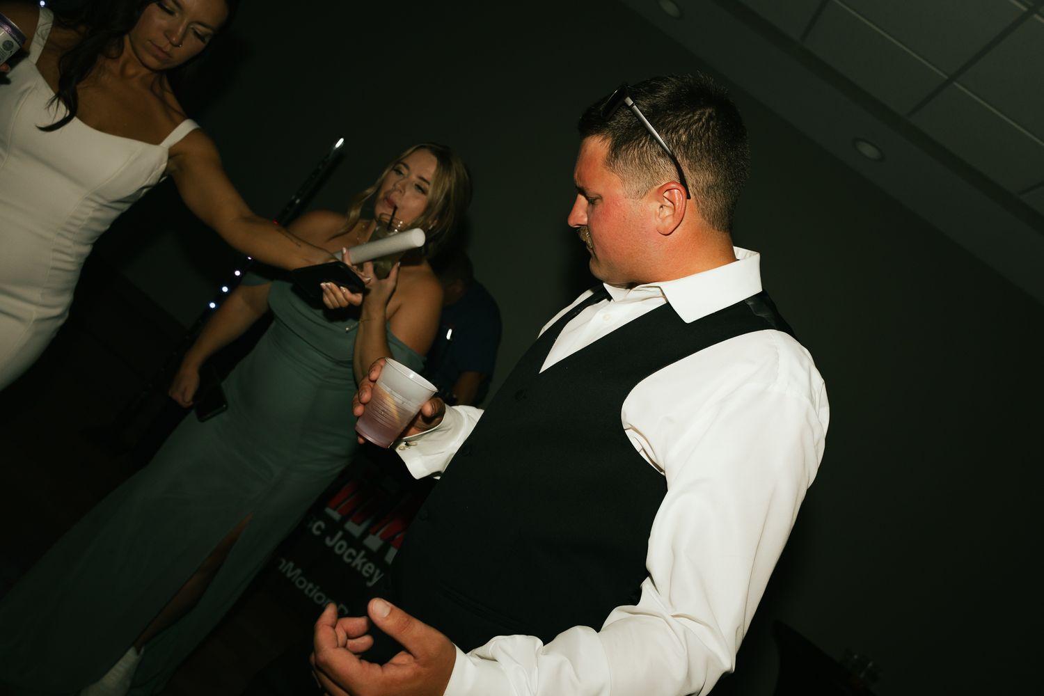 A party guest in formal attire holds drinks while entertaining others at an event.