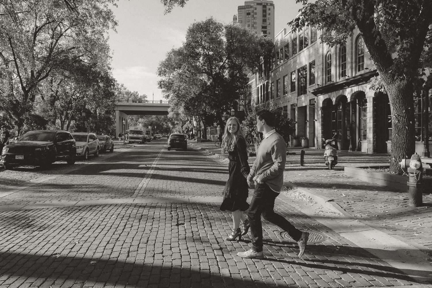 Vintage black and white photo of a cobblestone street with historic buildings and trees in an urban setting.