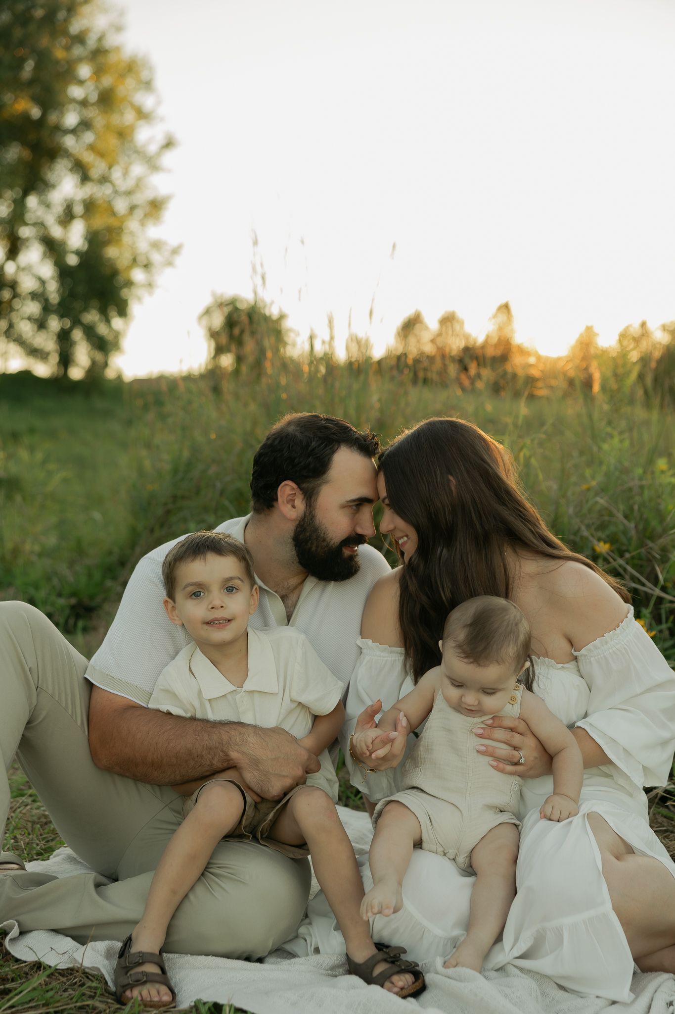 Family in white outfits sharing tender moments during sunset outdoor photo session.