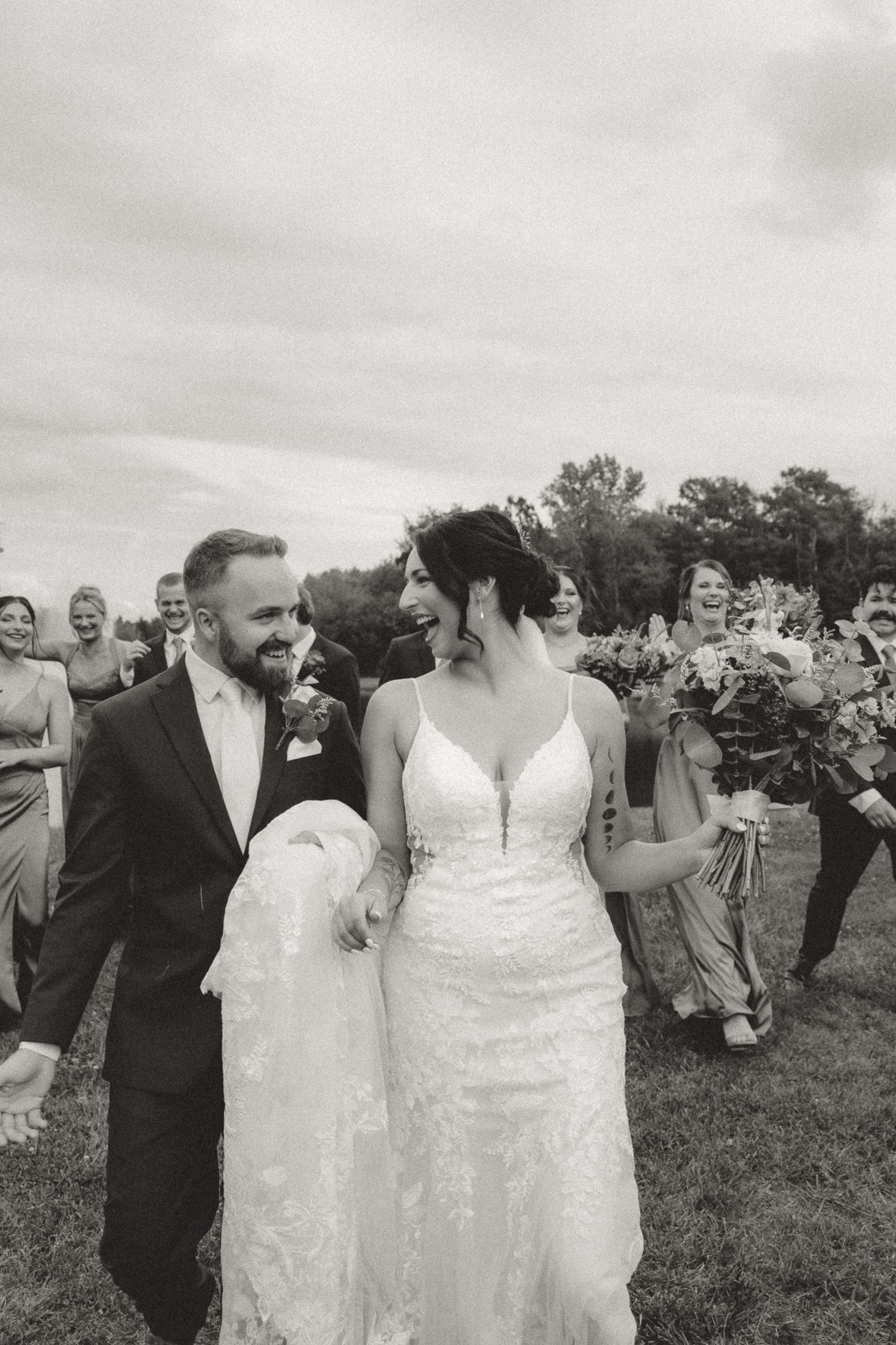 Wedding party celebrates outdoors with guests in a grassy field.