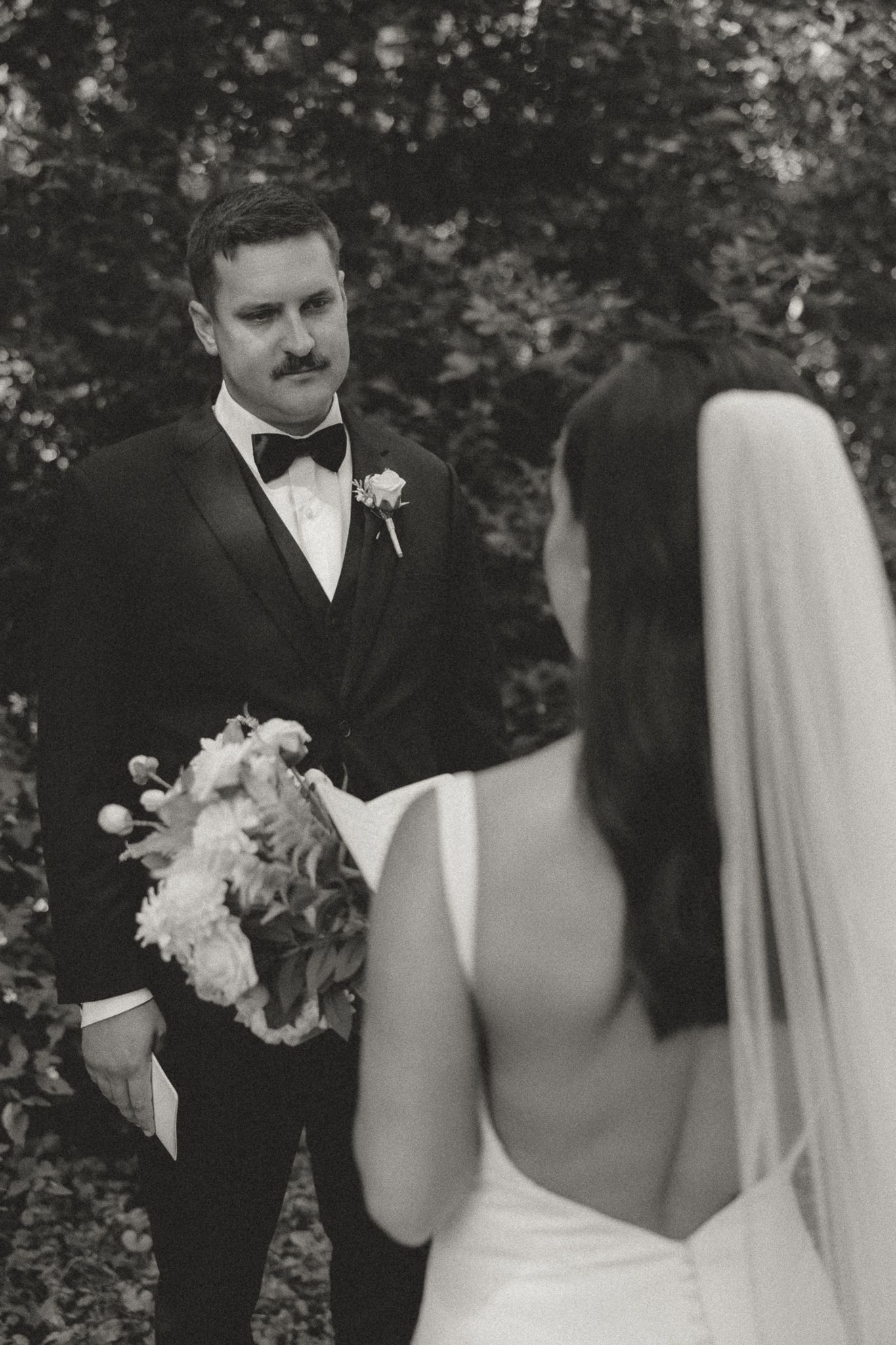 Black and white wedding photos showing first look between couple with floral bouquet.