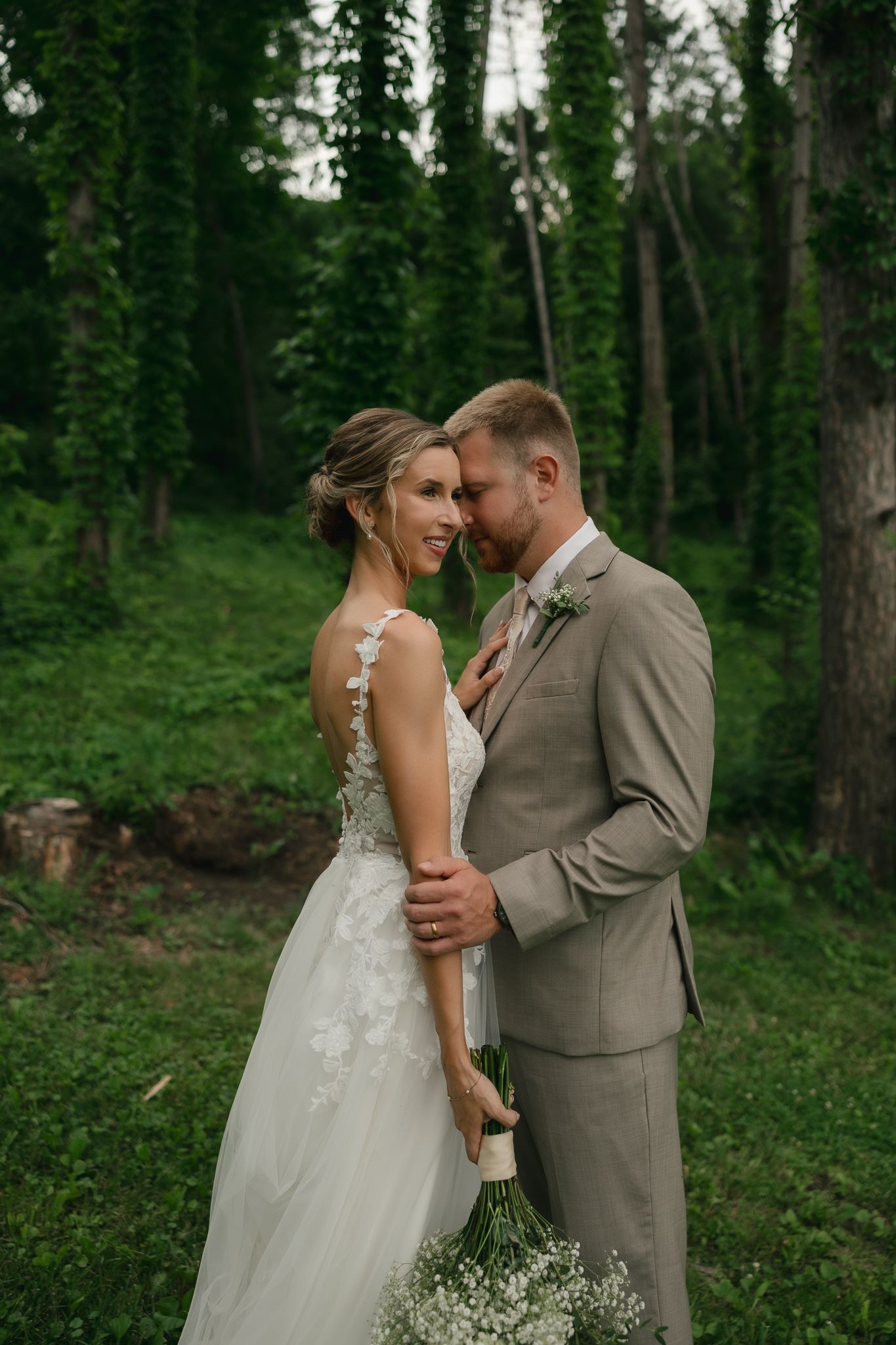 A romantic wedding moment captured in a lush forest setting with a white gown and tan suit.