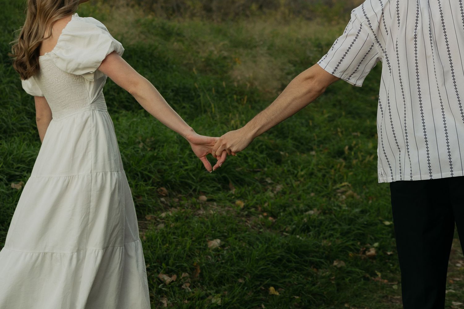 Couple in white outfits holding hands during romantic outdoor photoshoot.