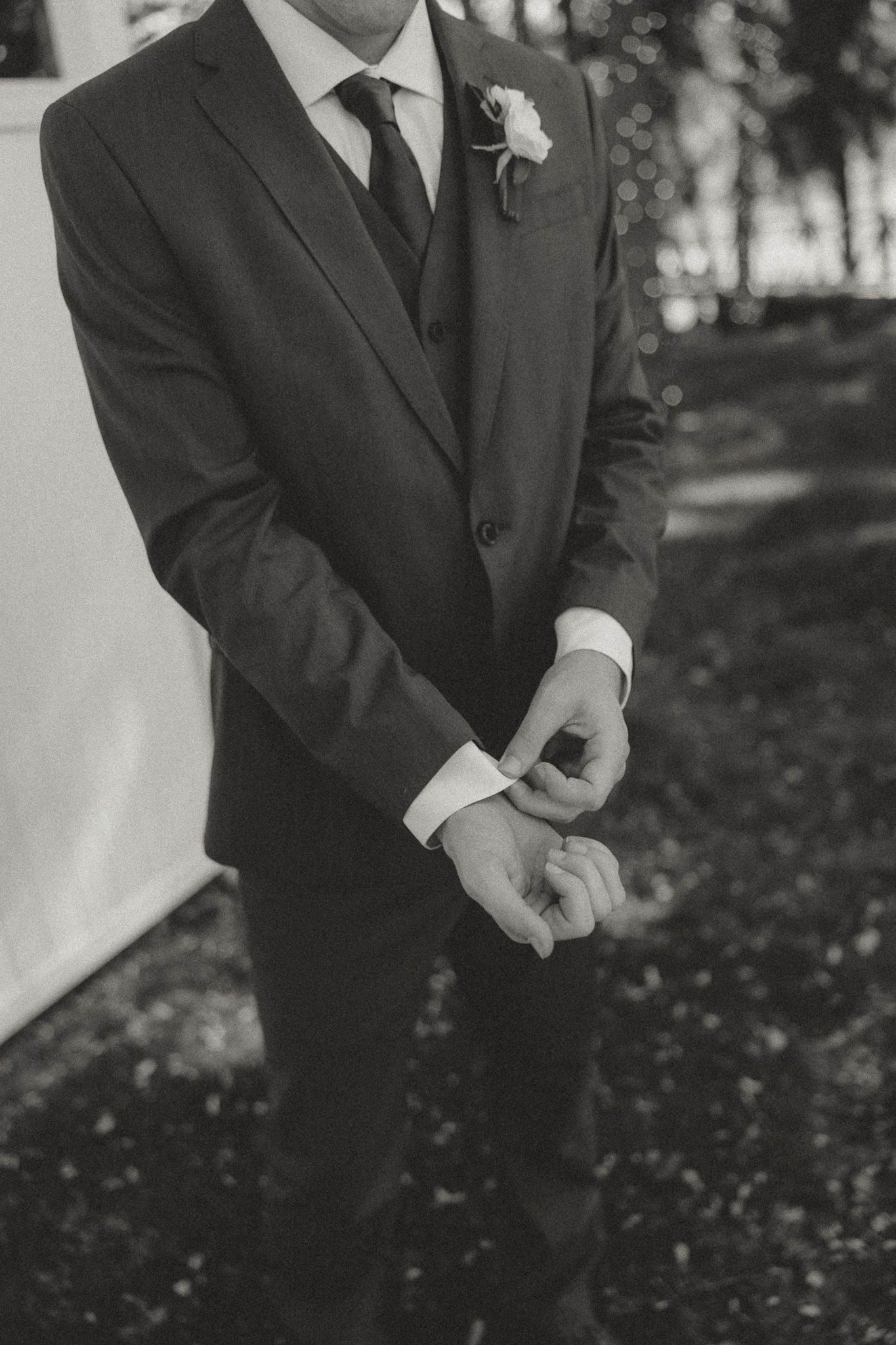 Black and white detail shot of groom adjusting cufflinks while wearing classic suit.