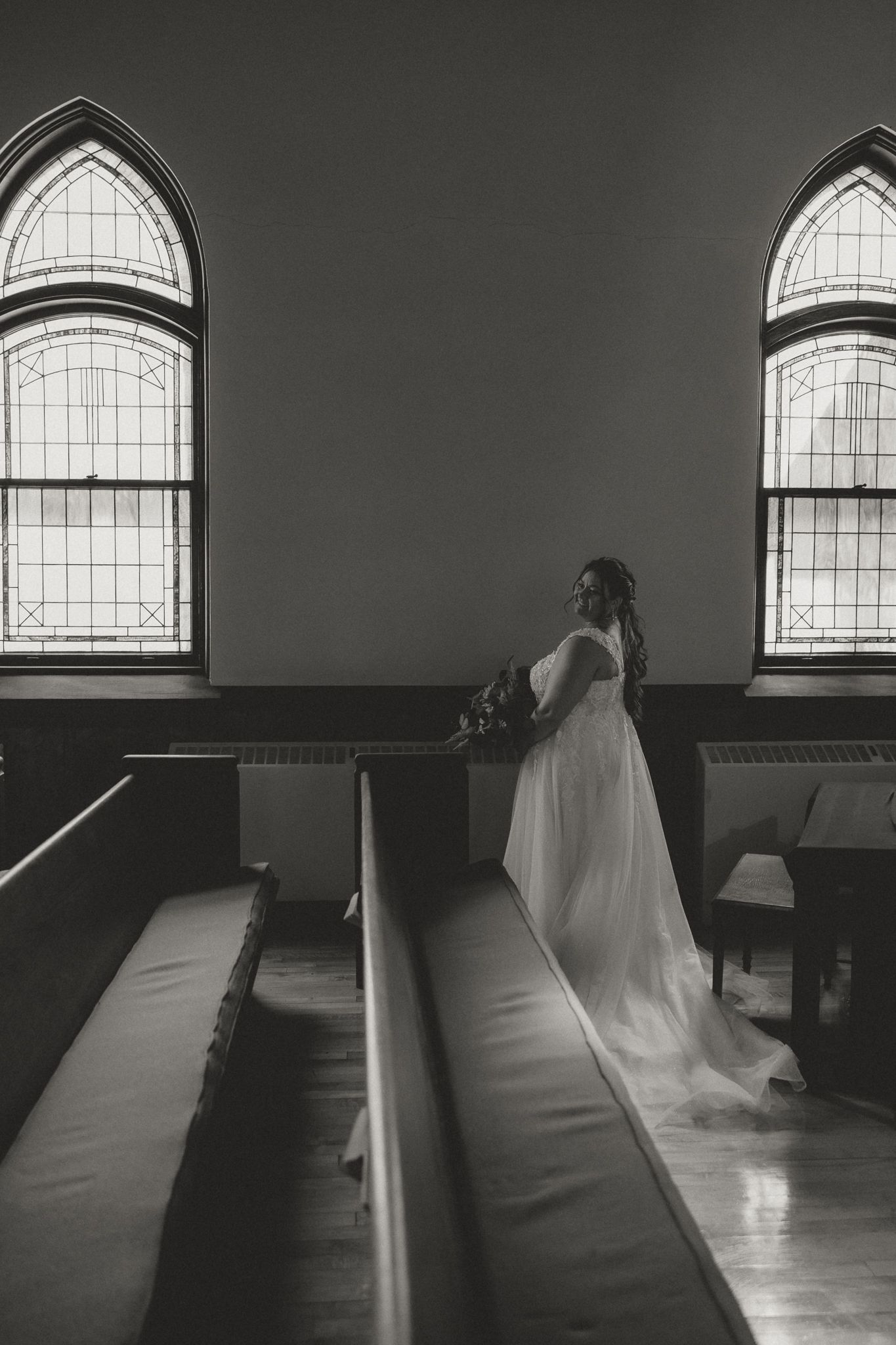 Black and white church interior with arched stained glass windows and empty pews.