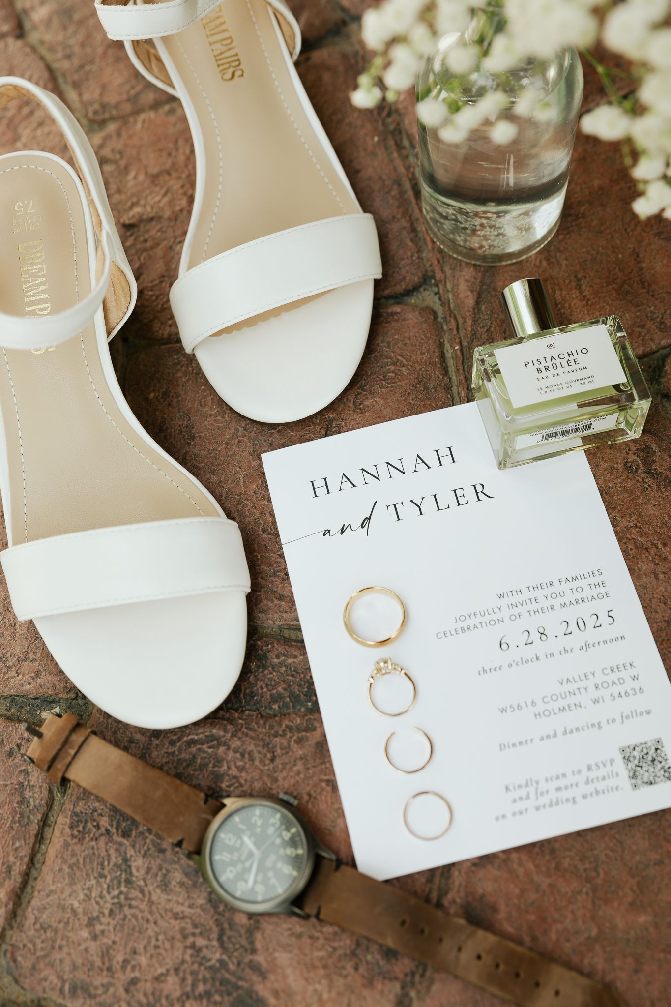 Wedding invitation suite with rings and white flowers displayed on a rustic stone surface.