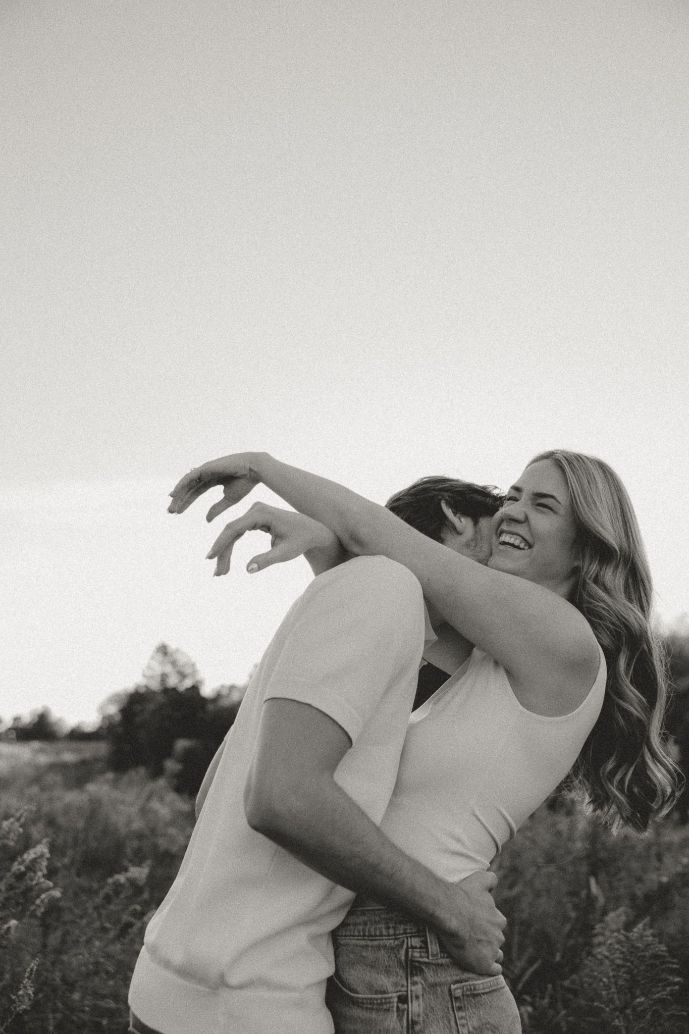 Black and white photo of a joyful couple sharing a playful embrace outdoors.