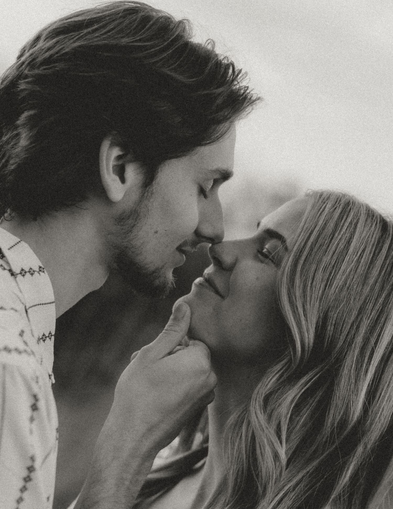 Black and white portrait of a couple sharing a tender moment outdoors.