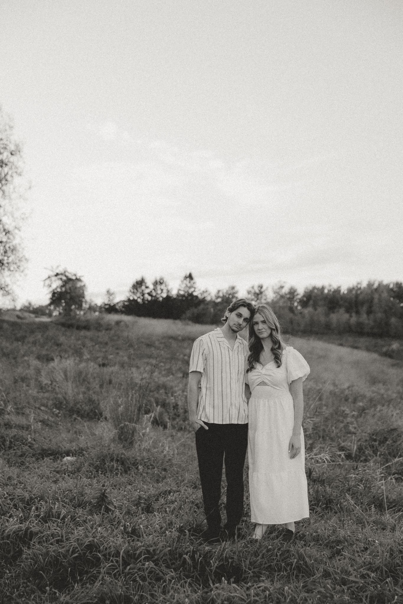 A black and white portrait of a couple standing together in a meadow.