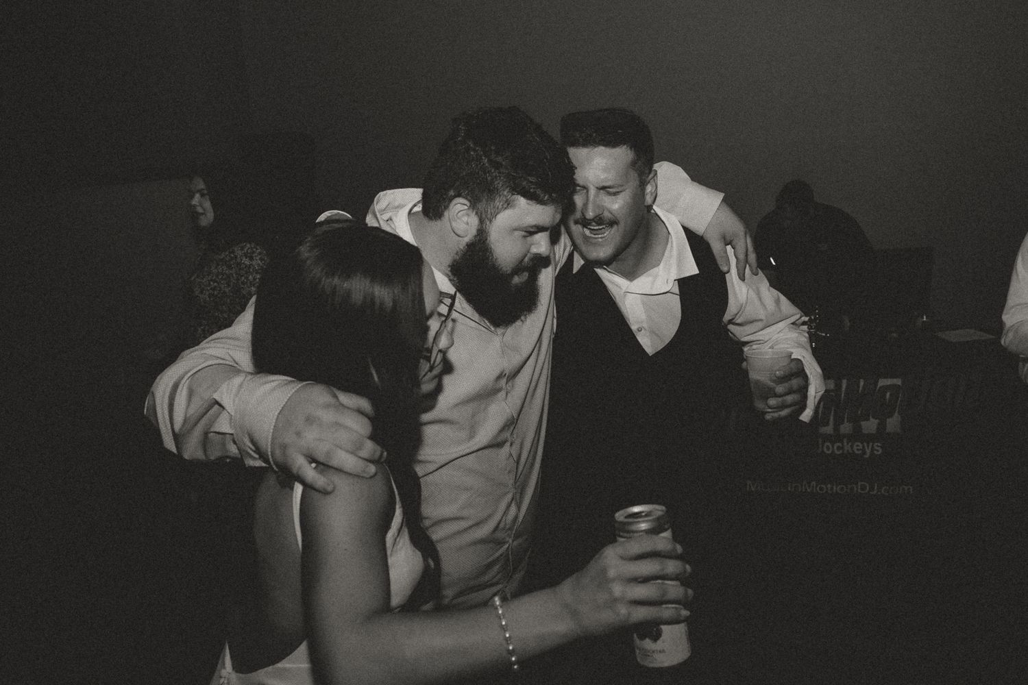 Friends gather closely in black and white photo while sharing drinks at a celebration.