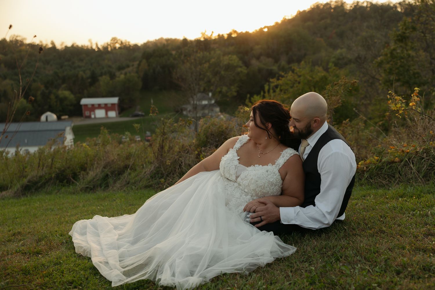 Bride and groom share romantic moments on a grassy hillside during sunset.