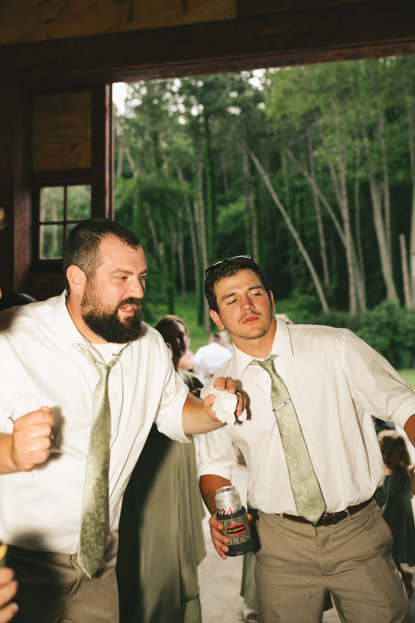 Groomsmen in light colored suits celebrating at rustic venue.