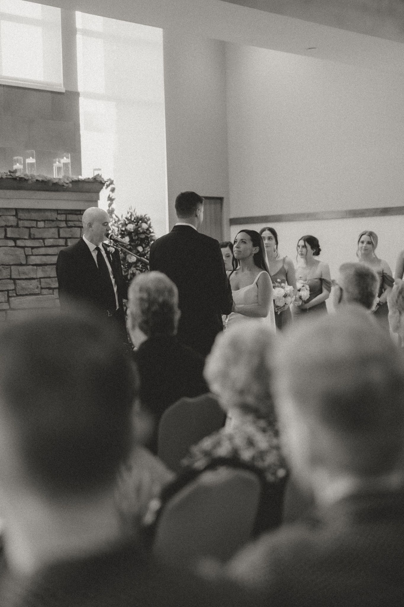 Wedding ceremony guests seated in rows at an indoor venue with white walls and stone accents.