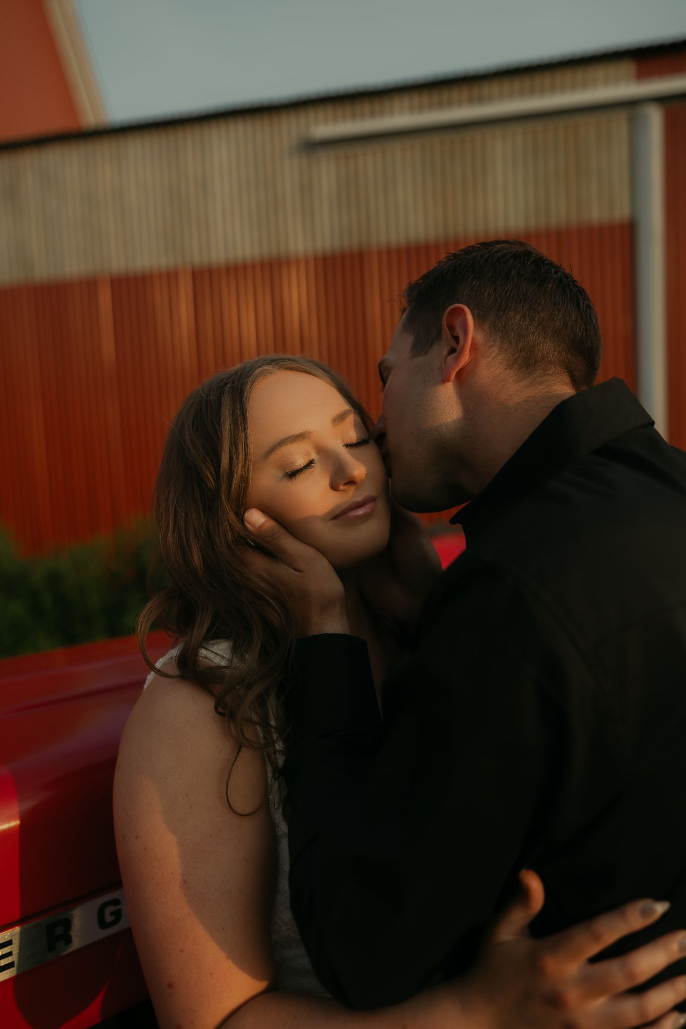 A romantic moment captured against a red barn backdrop during sunset.