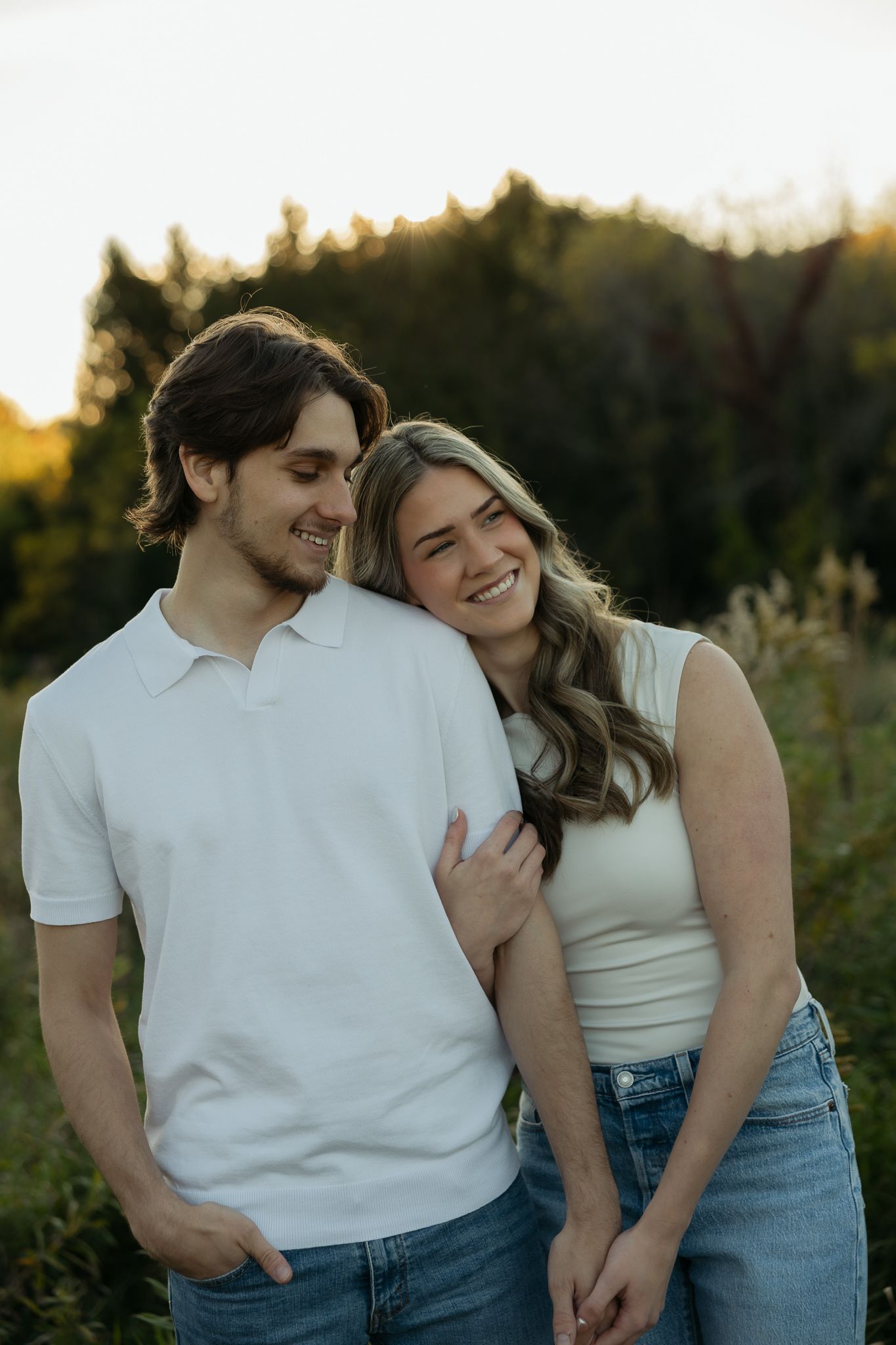 Couple in white shirts and jeans embrace during sunset photoshoot.