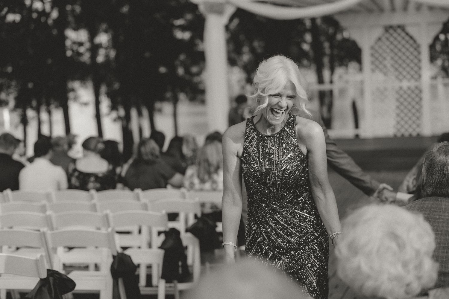 Wedding guests seated in white chairs during an outdoor ceremony.