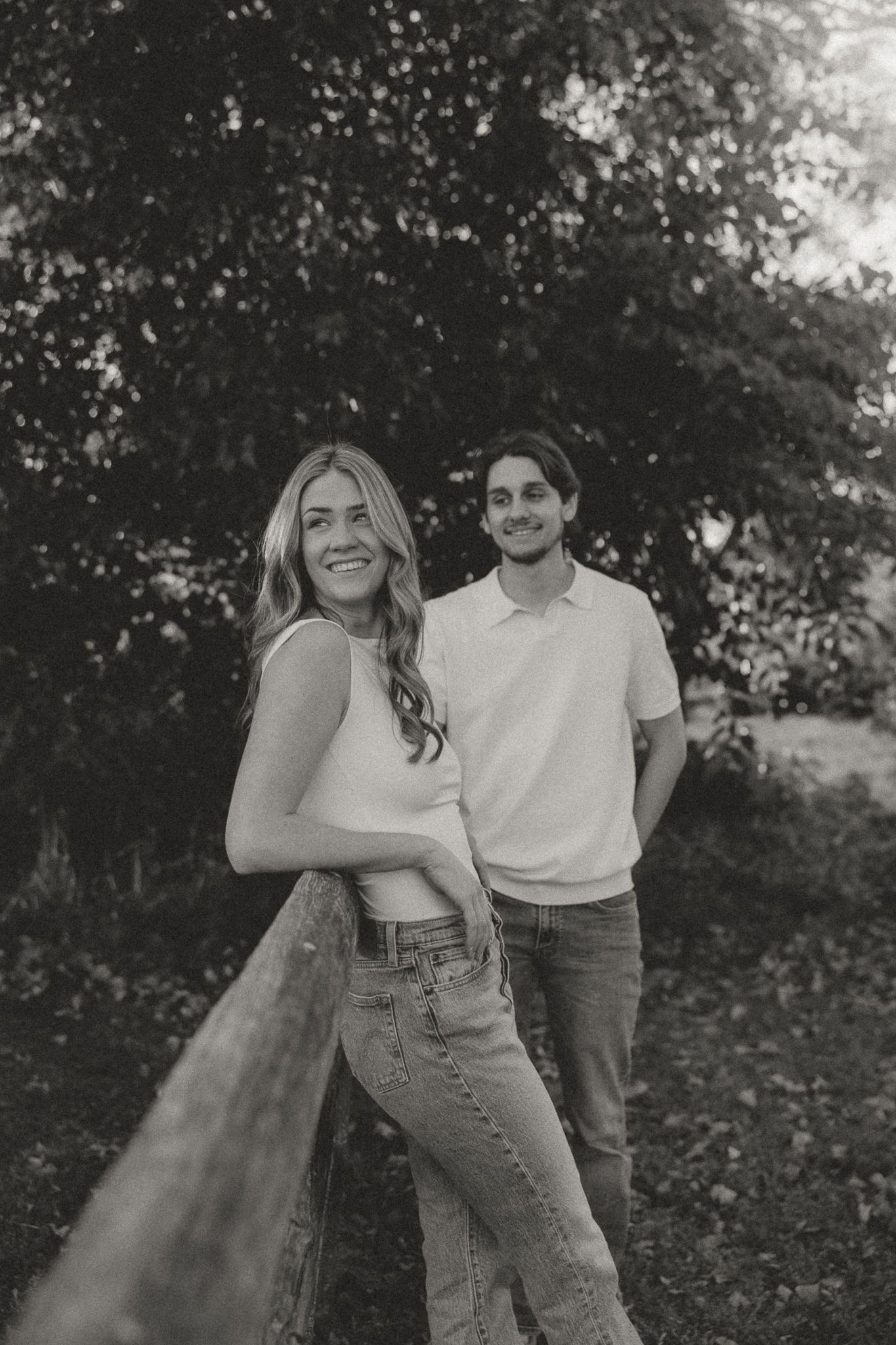 Black and white photo of a couple posing casually by a wooden fence.