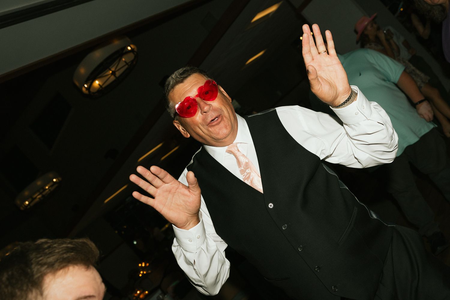 Wedding guests dance and celebrate at a lively reception party with dark lighting and festive atmosphere.