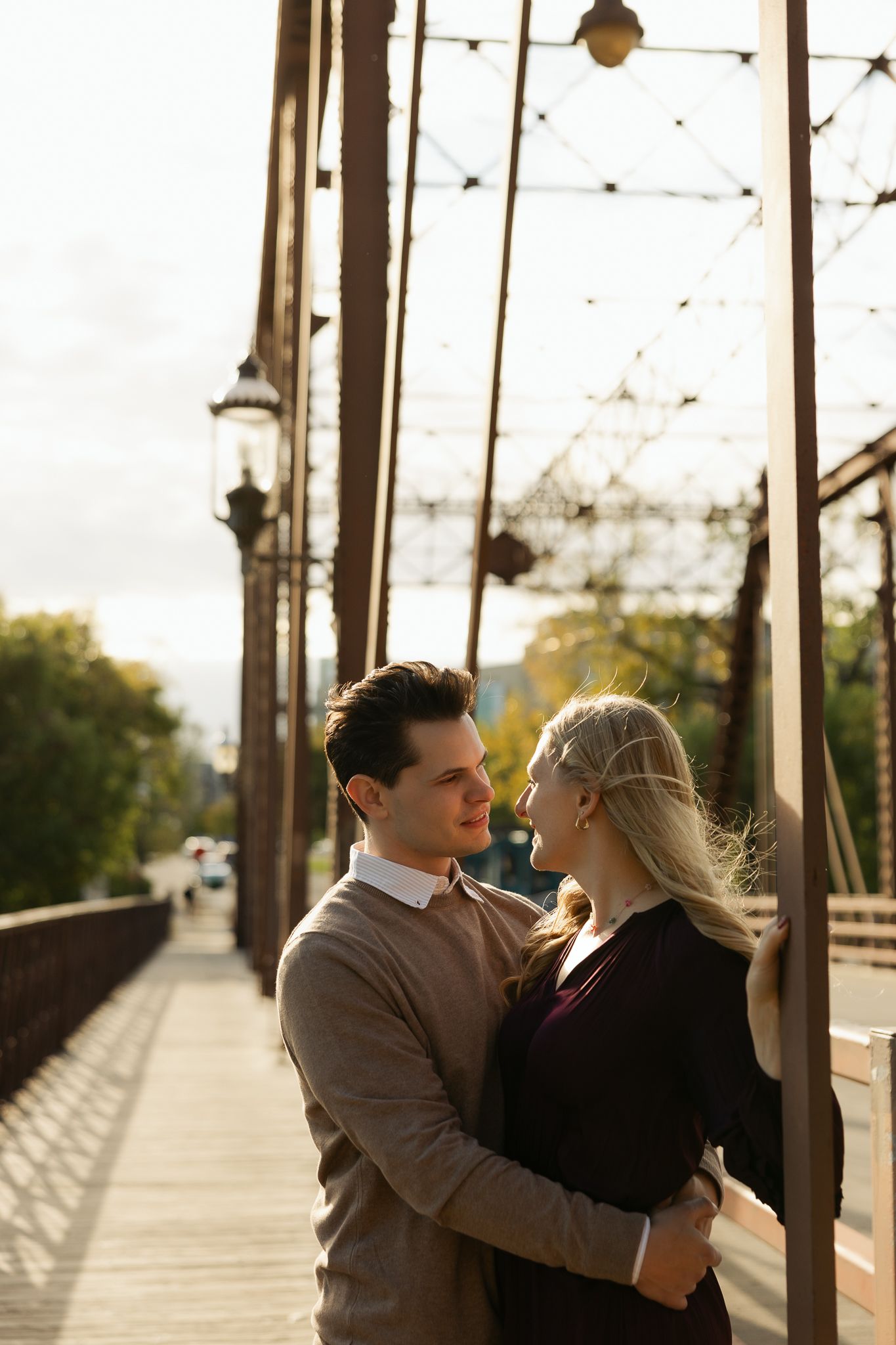 Sunset photo of couple sharing an intimate moment on a bridge with industrial elements.
