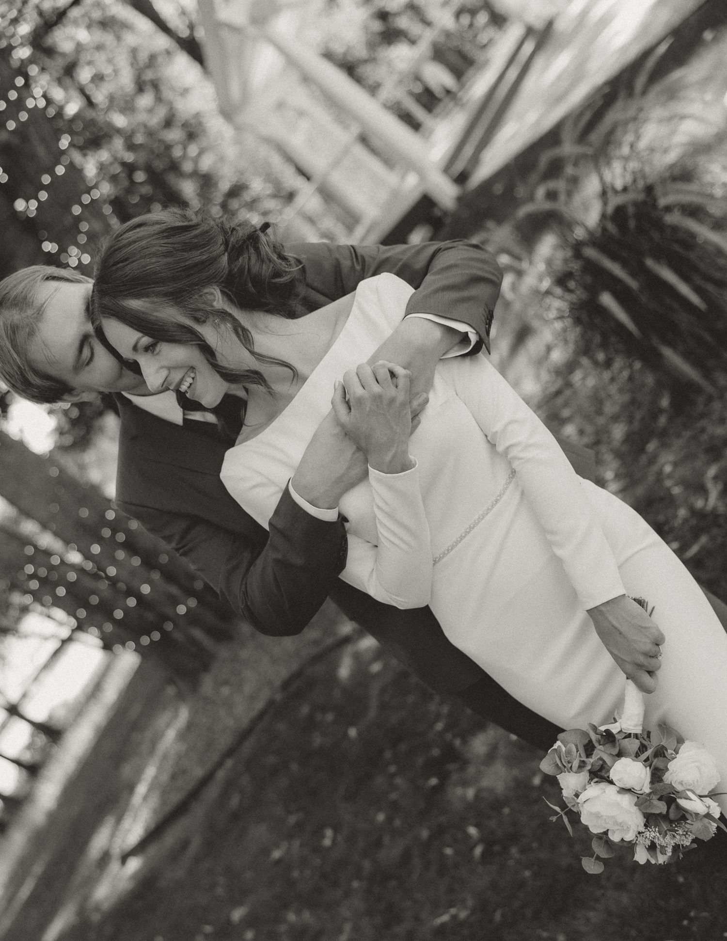 A black and white romantic wedding photo showing a couple dancing outdoors.