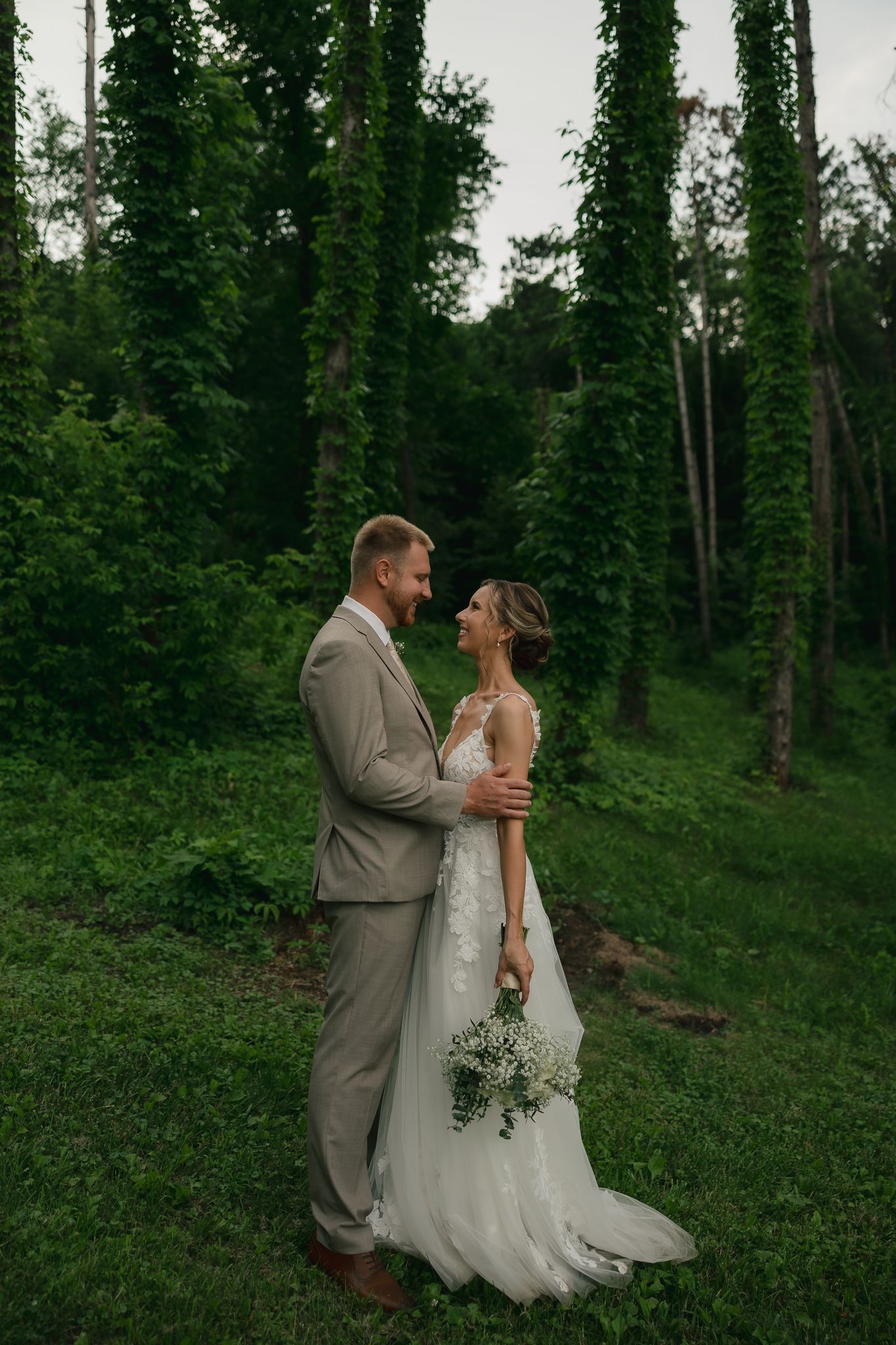 Newlyweds share an intimate moment surrounded by evergreen trees and natural greenery.