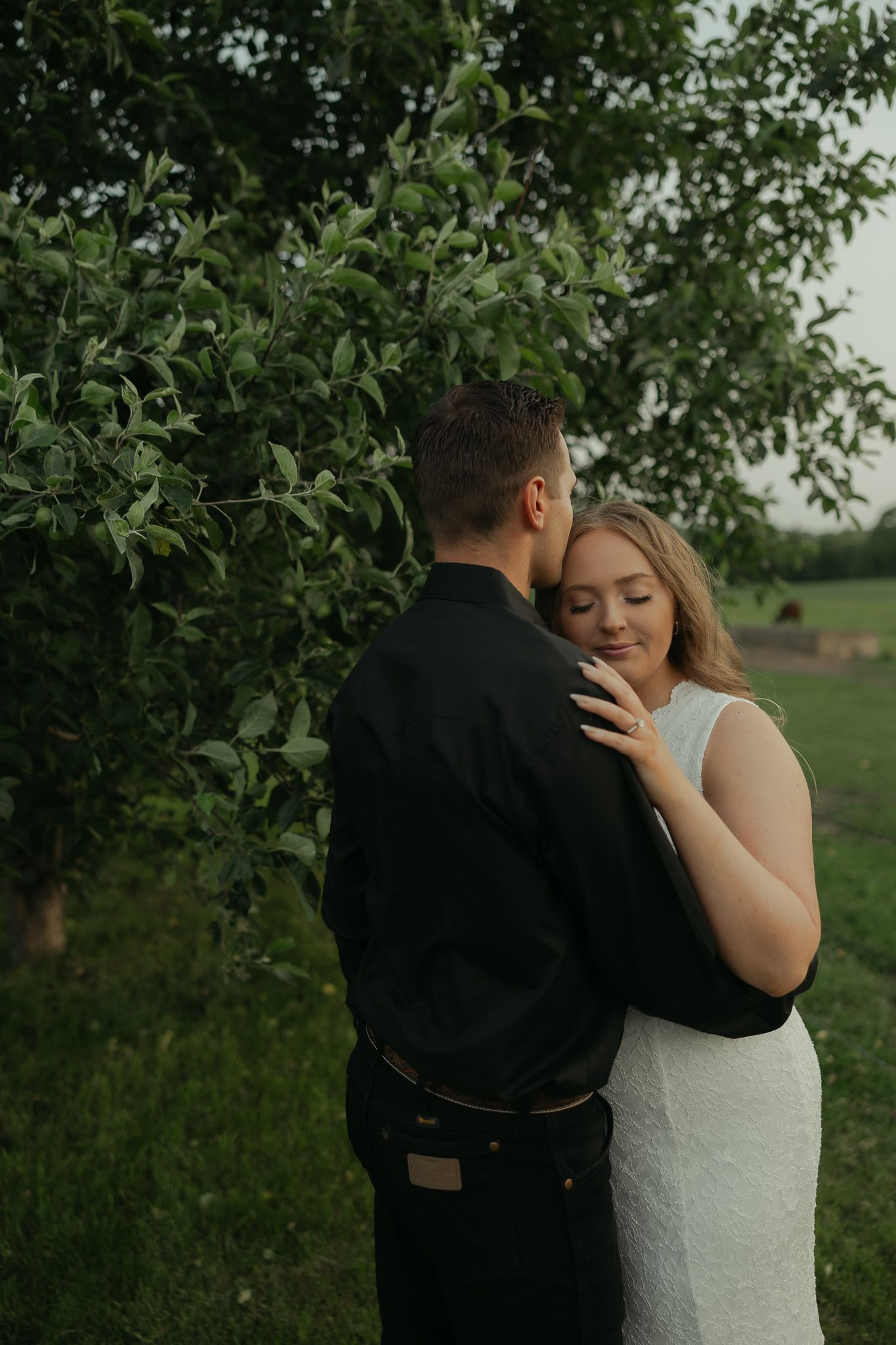 A tender moment between a couple among green foliage during an outdoor portrait session.