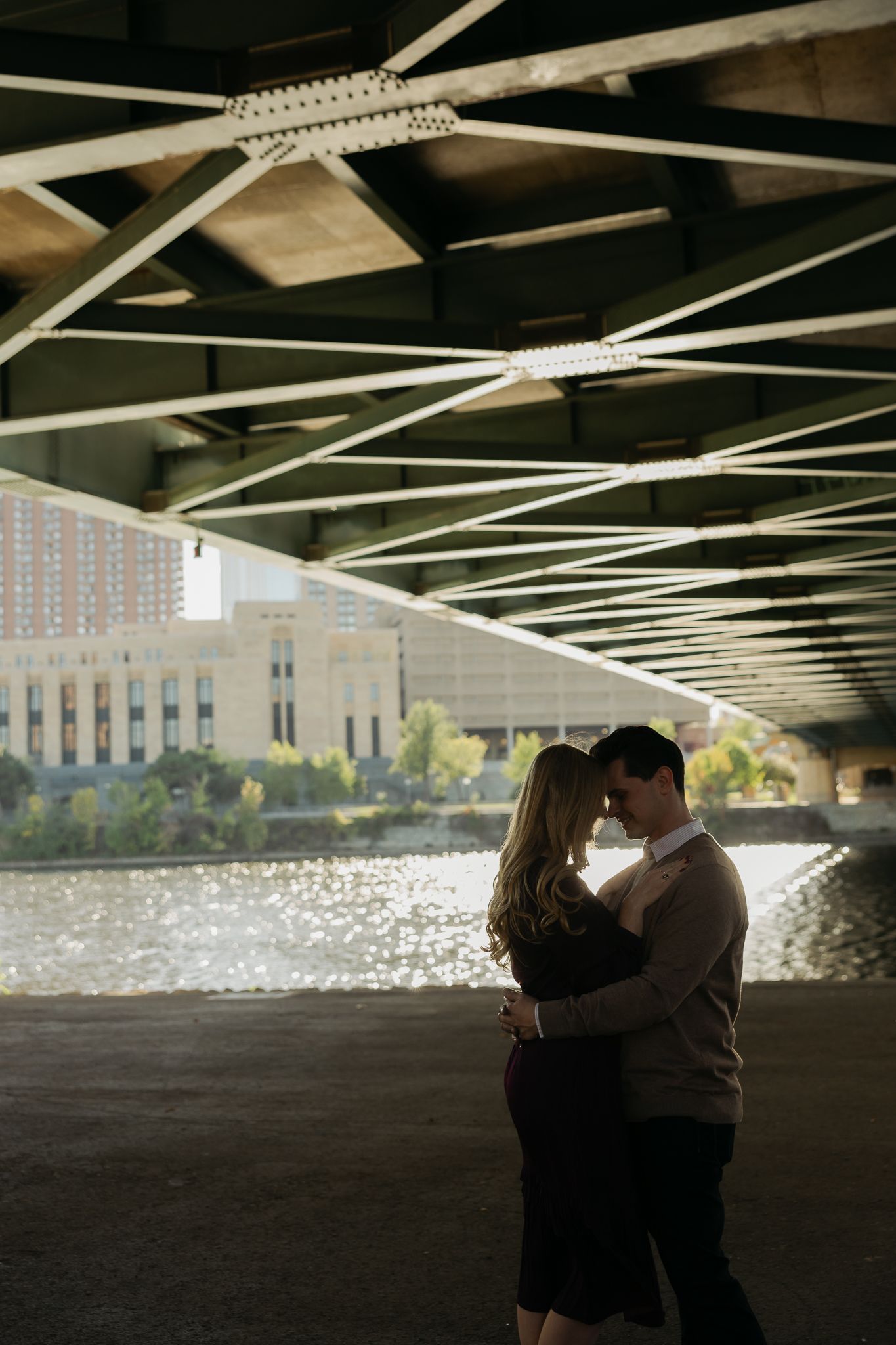 Silhouetted couple sharing romantic moments under a bridge with water reflections.