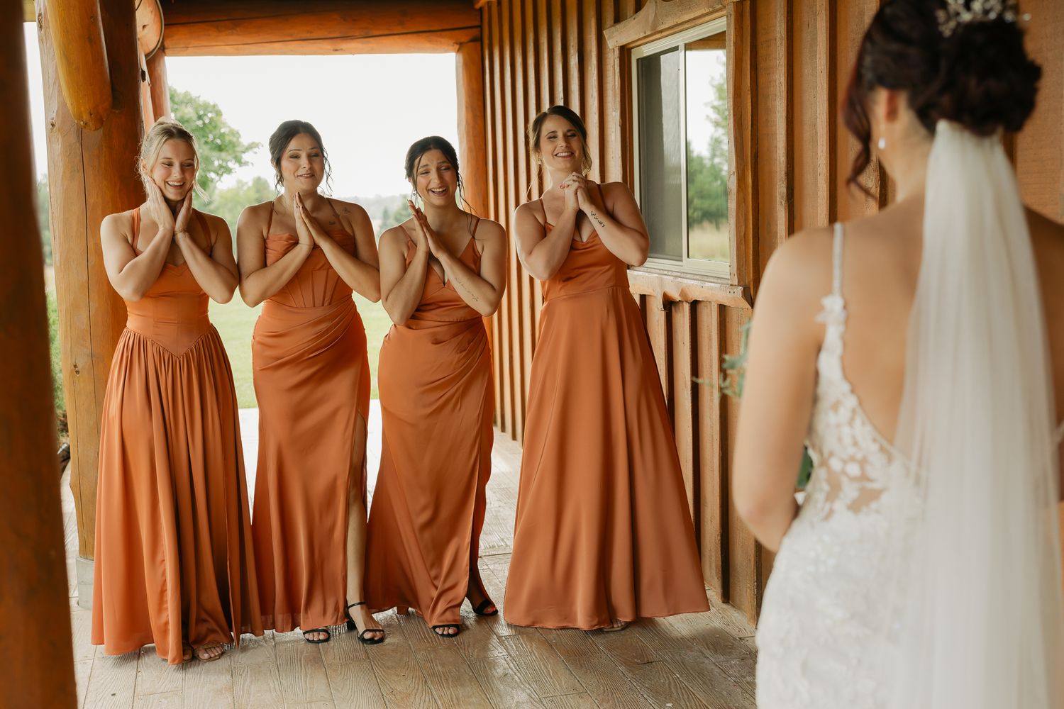Bridesmaids in rust-colored dresses pose together on a wooden porch.