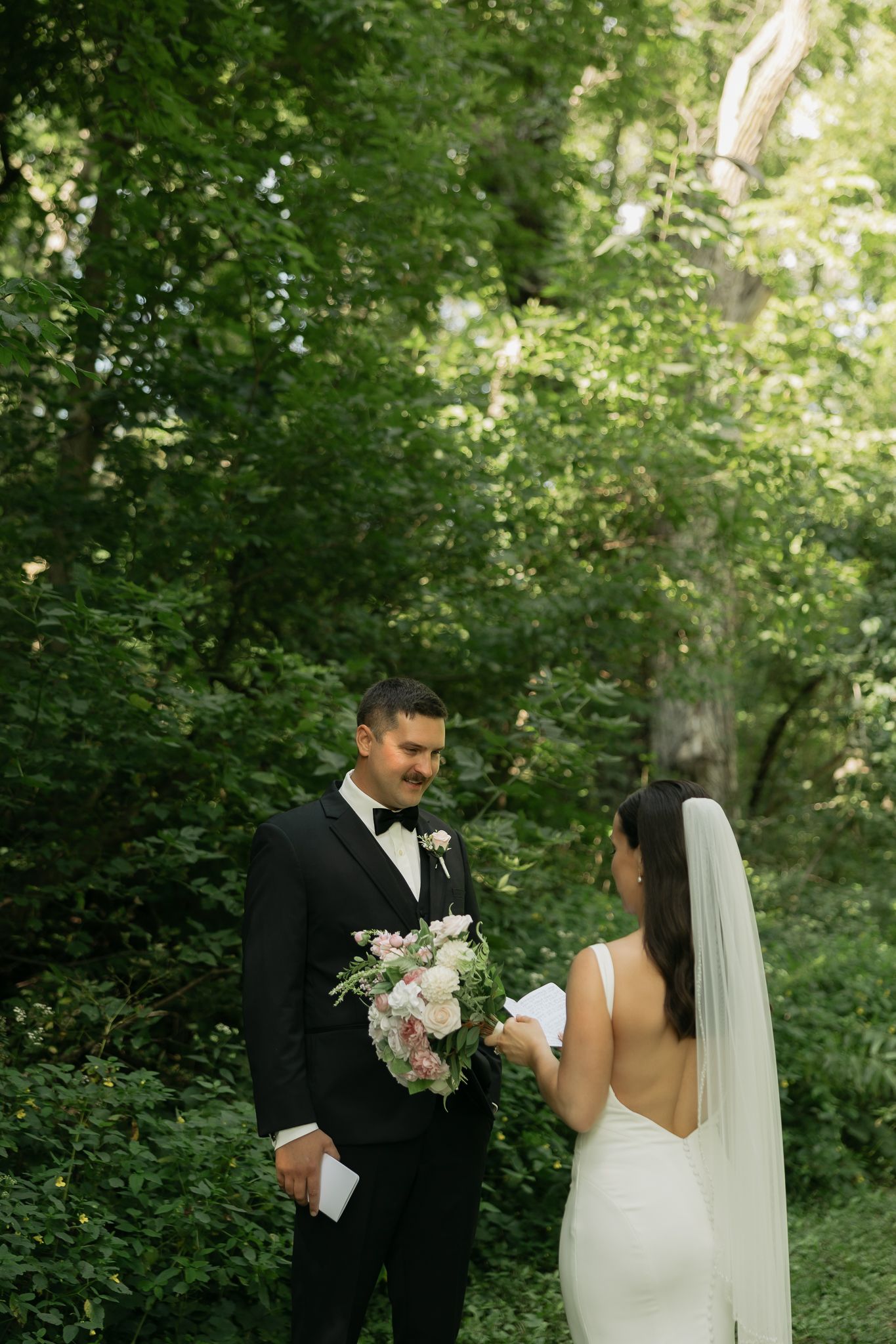 A romantic wedding moment captured in a lush forest setting with a beautiful bouquet of pink and white flowers.
