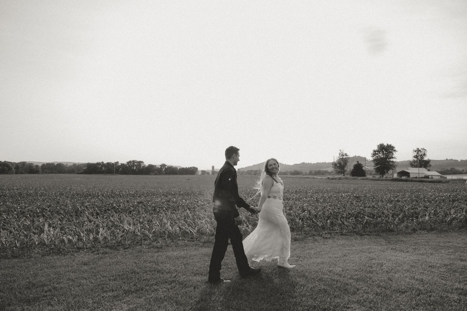 A couple shares a romantic moment in a vast rural field at golden hour.