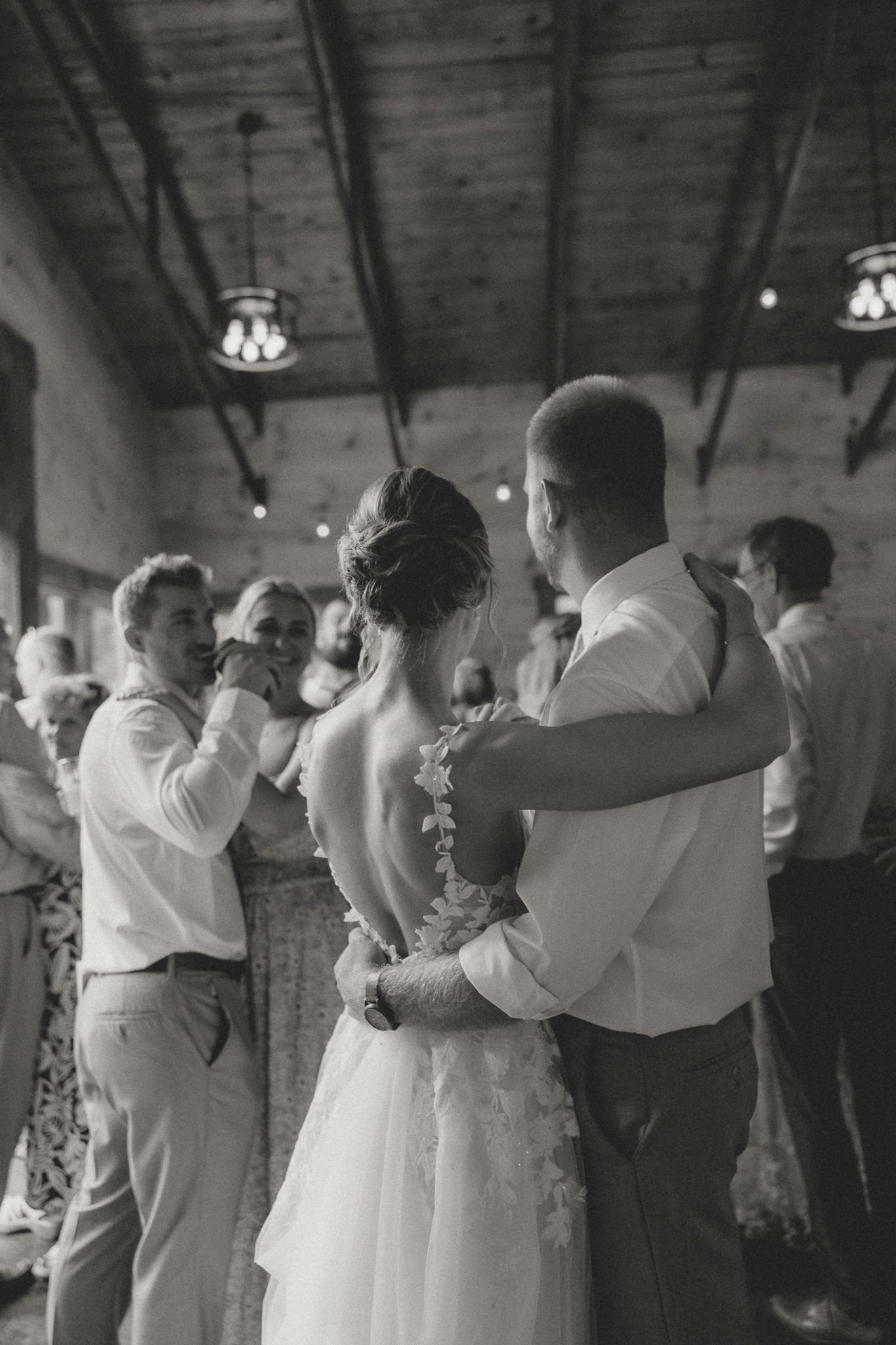 Black and white photo of guests dancing together at a wedding reception in a rustic venue.