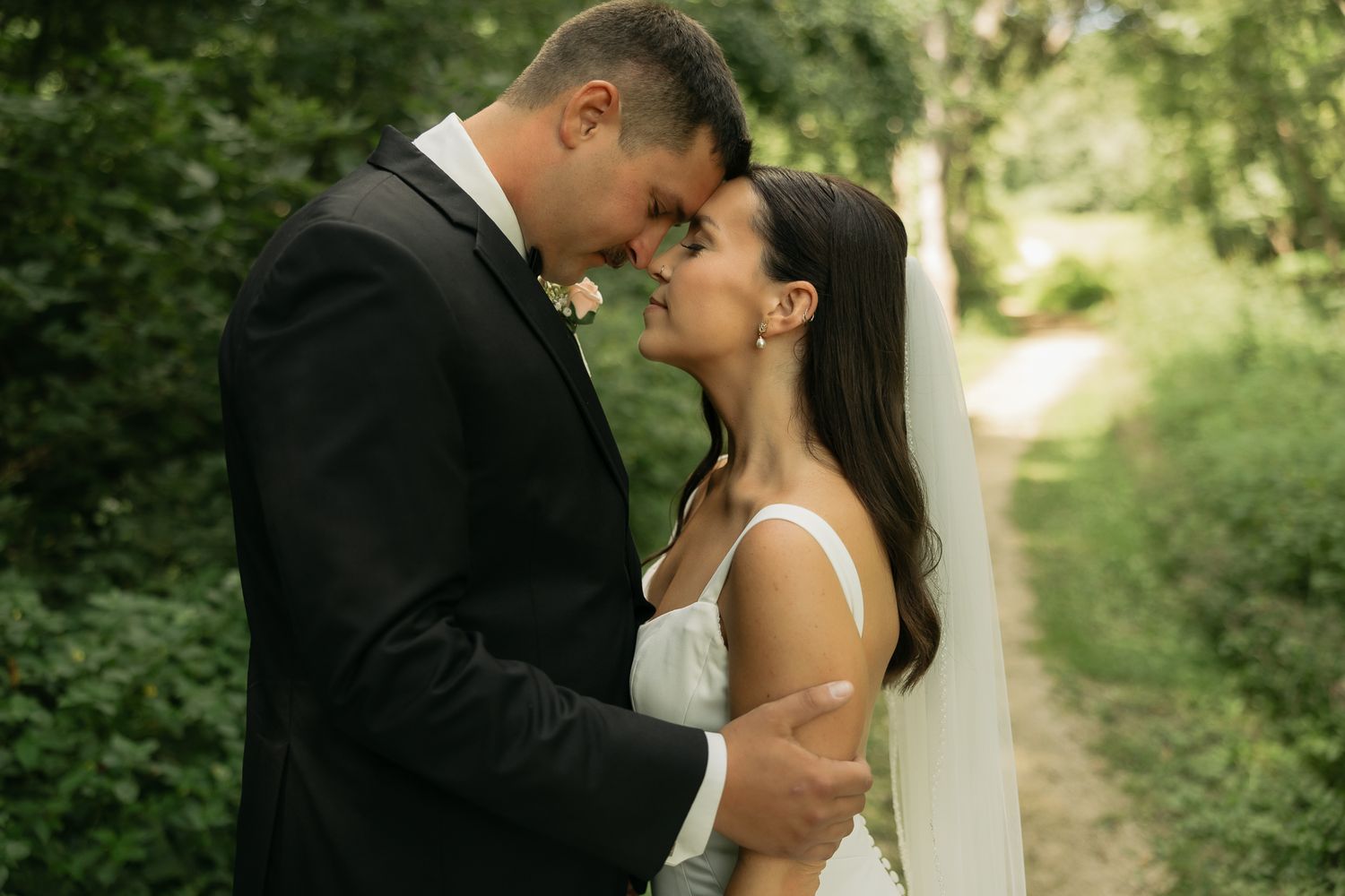 Romantic forest wedding photo showing tender embrace between newlyweds on a woodland path.