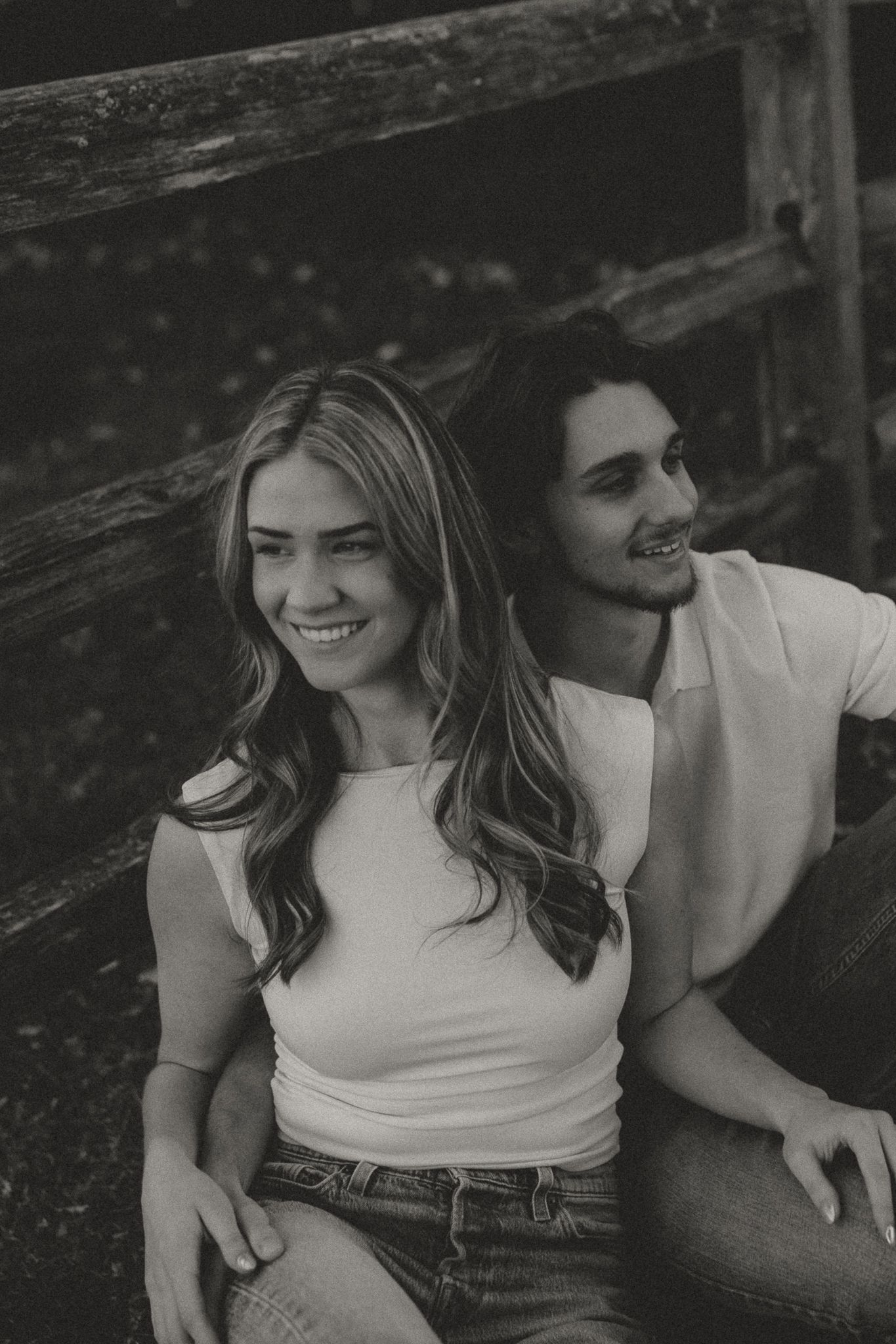 Casual outdoor couple's photoshoot showing genuine laughter and connection by rustic fence.