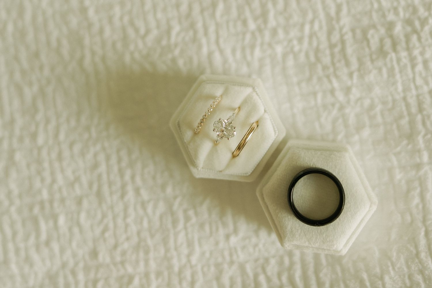 Wedding ring details arranged on textured white fabric with hexagonal design.