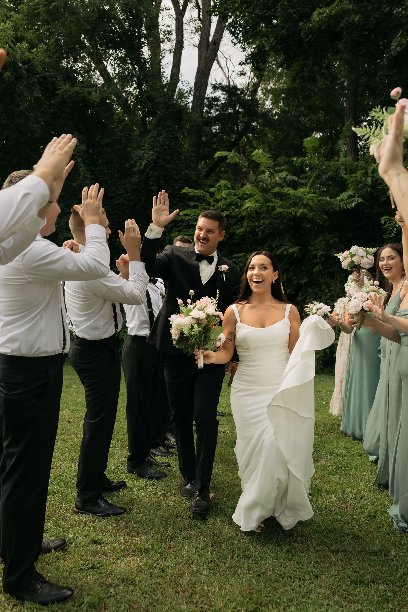 Wedding celebration with bridal party creating a joyful walkway tunnel outdoors.