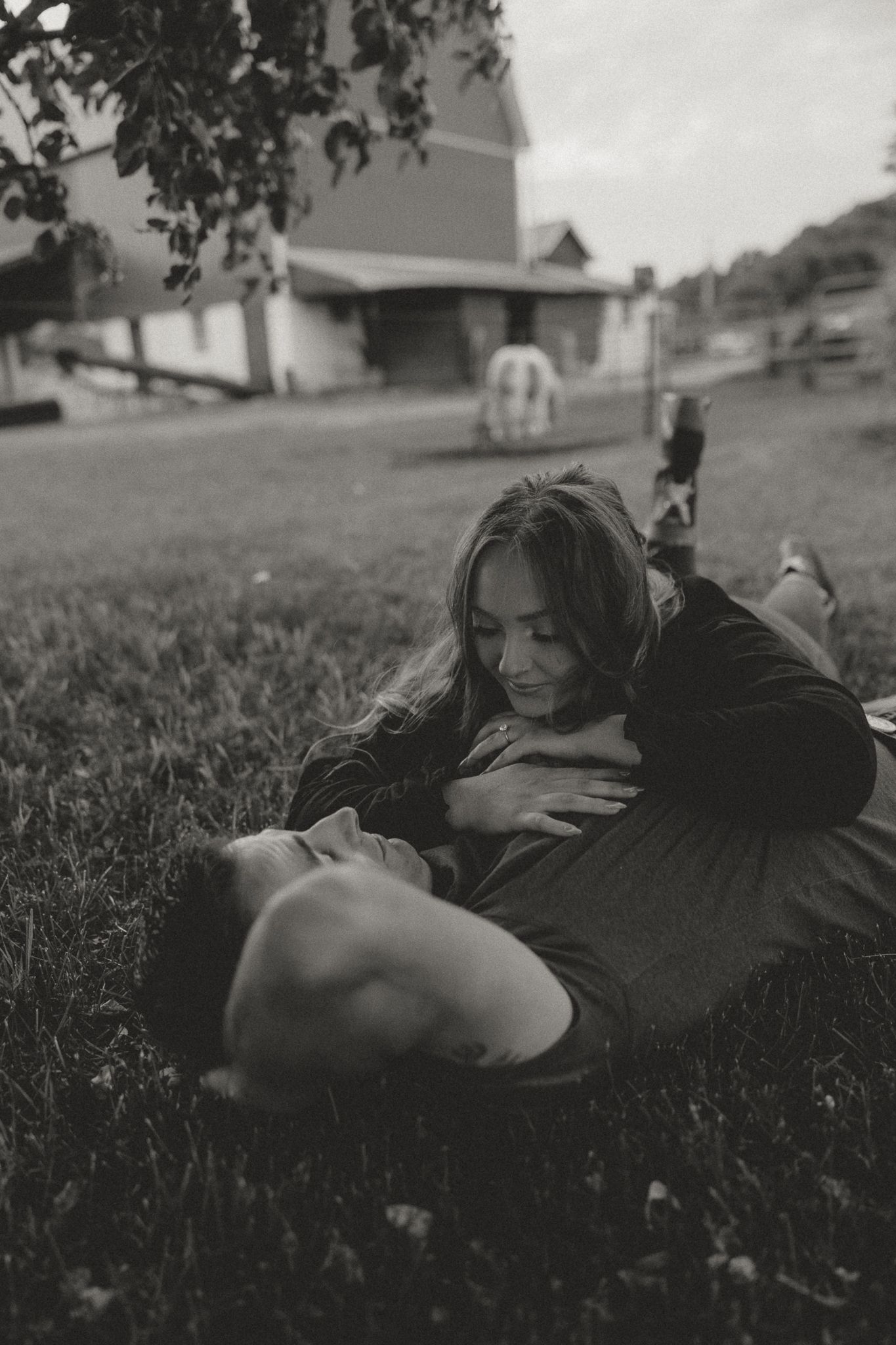 A couple shares an intimate moment while lying in black and white on grassy ground.