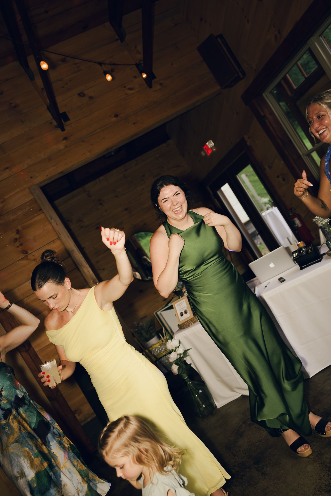 Wedding guests dancing and celebrating in colorful dresses at an indoor reception.