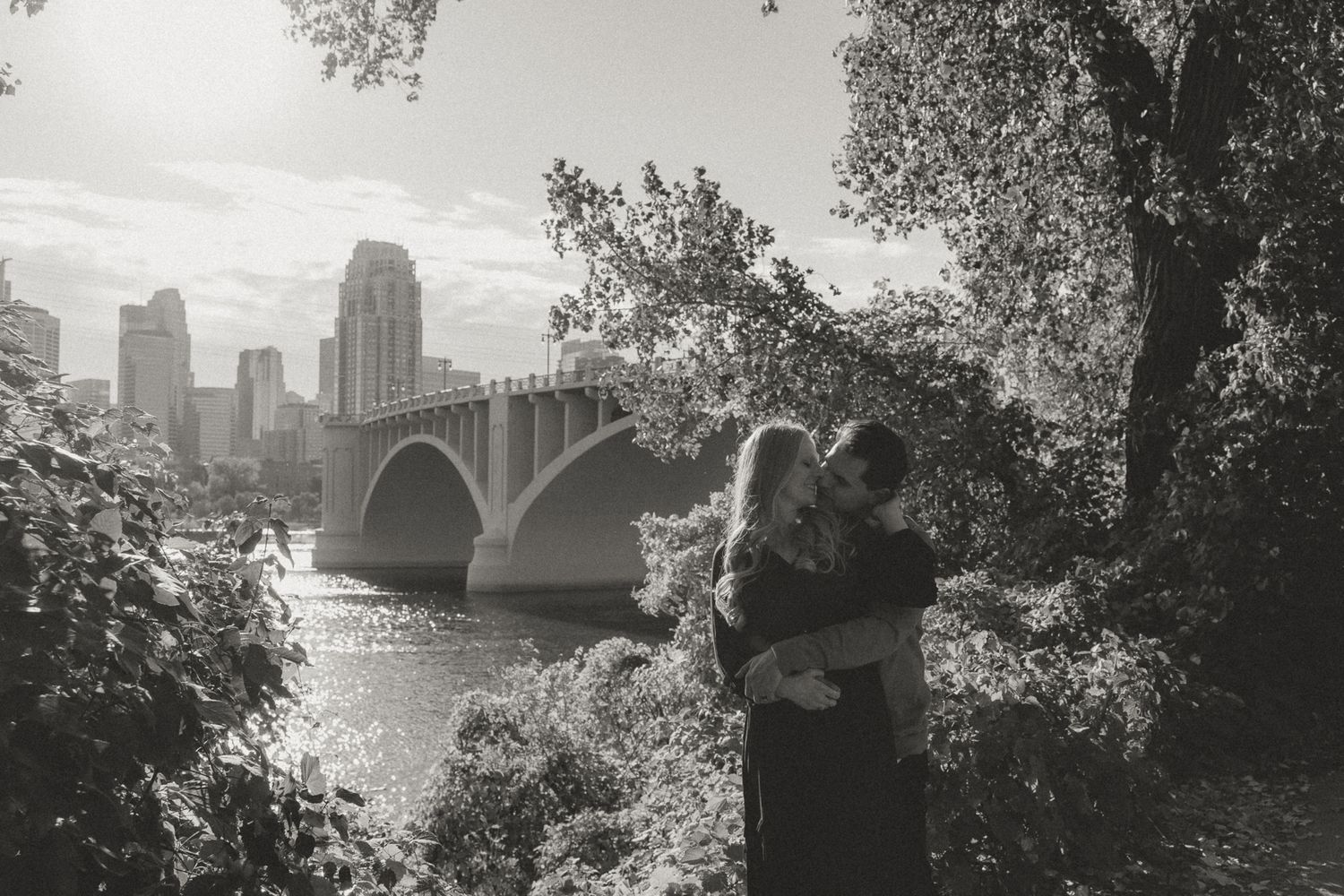 Silhouetted couple embracing near a bridge with city skyline in the background.