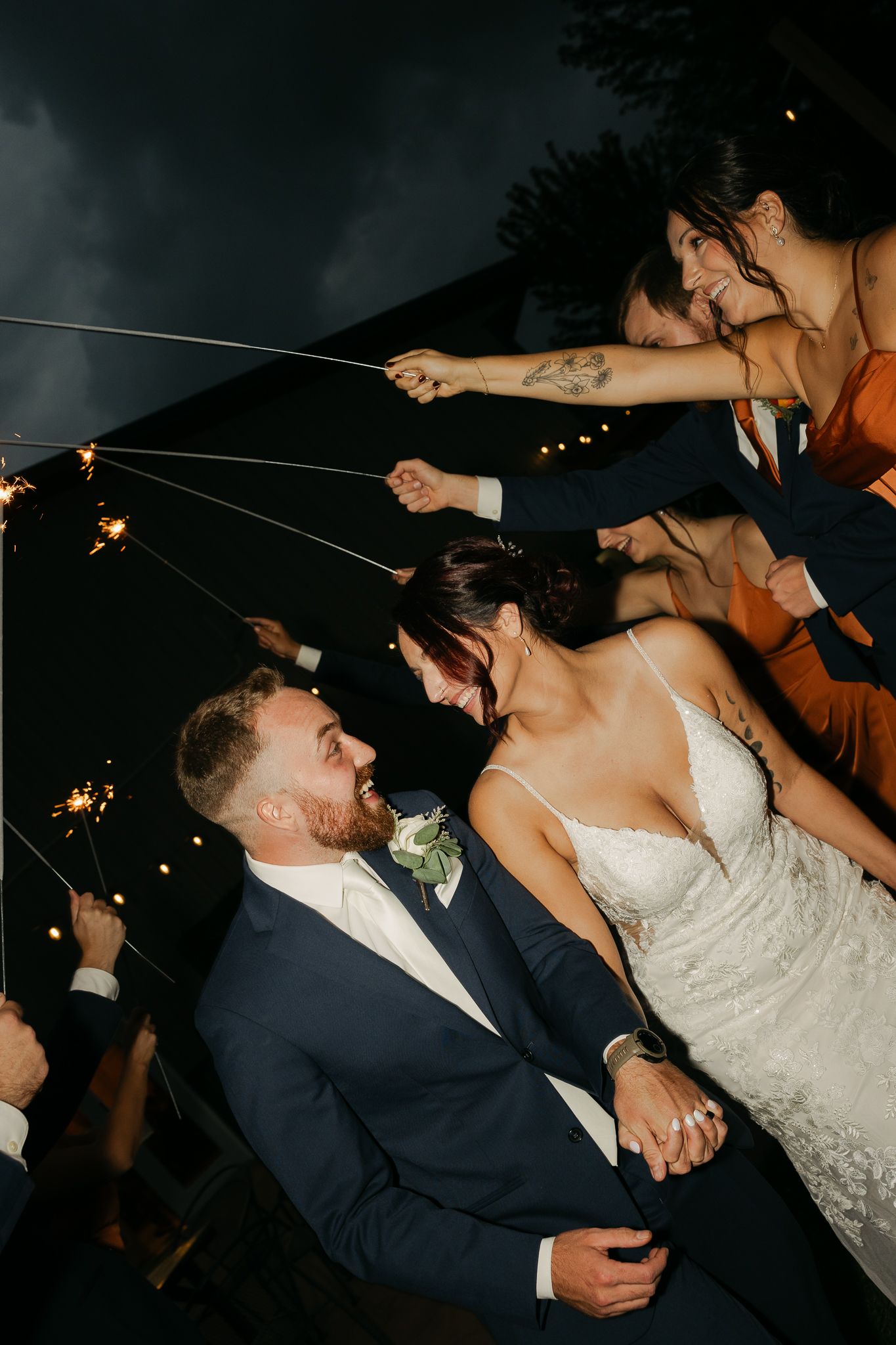 Joyful wedding celebration with sparklers illuminating the night as guests surround the newlyweds.
